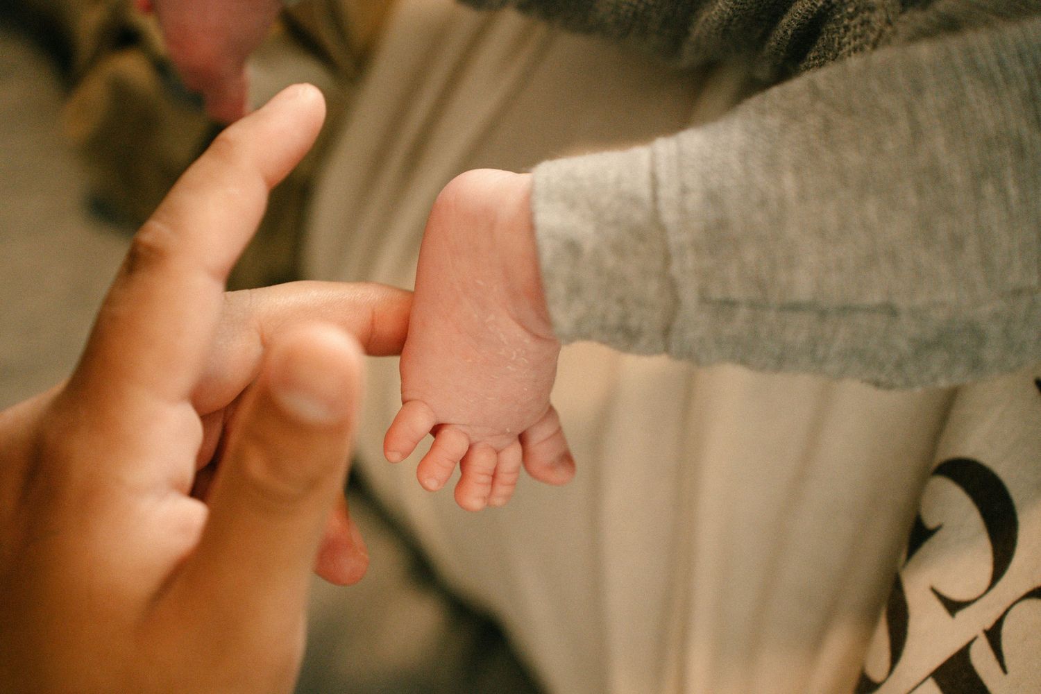 Close-up of adult finger gently touching tiny newborn baby foot in soft indoor light.