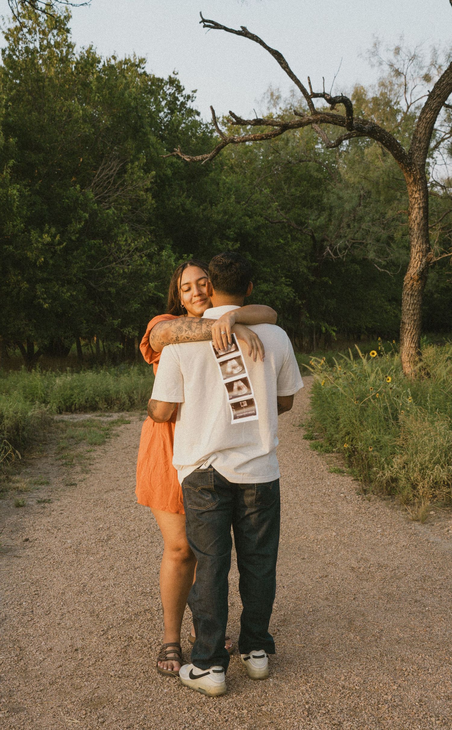 Happy couple embracing on a nature path while holding ultrasound photos to reveal pregnancy.