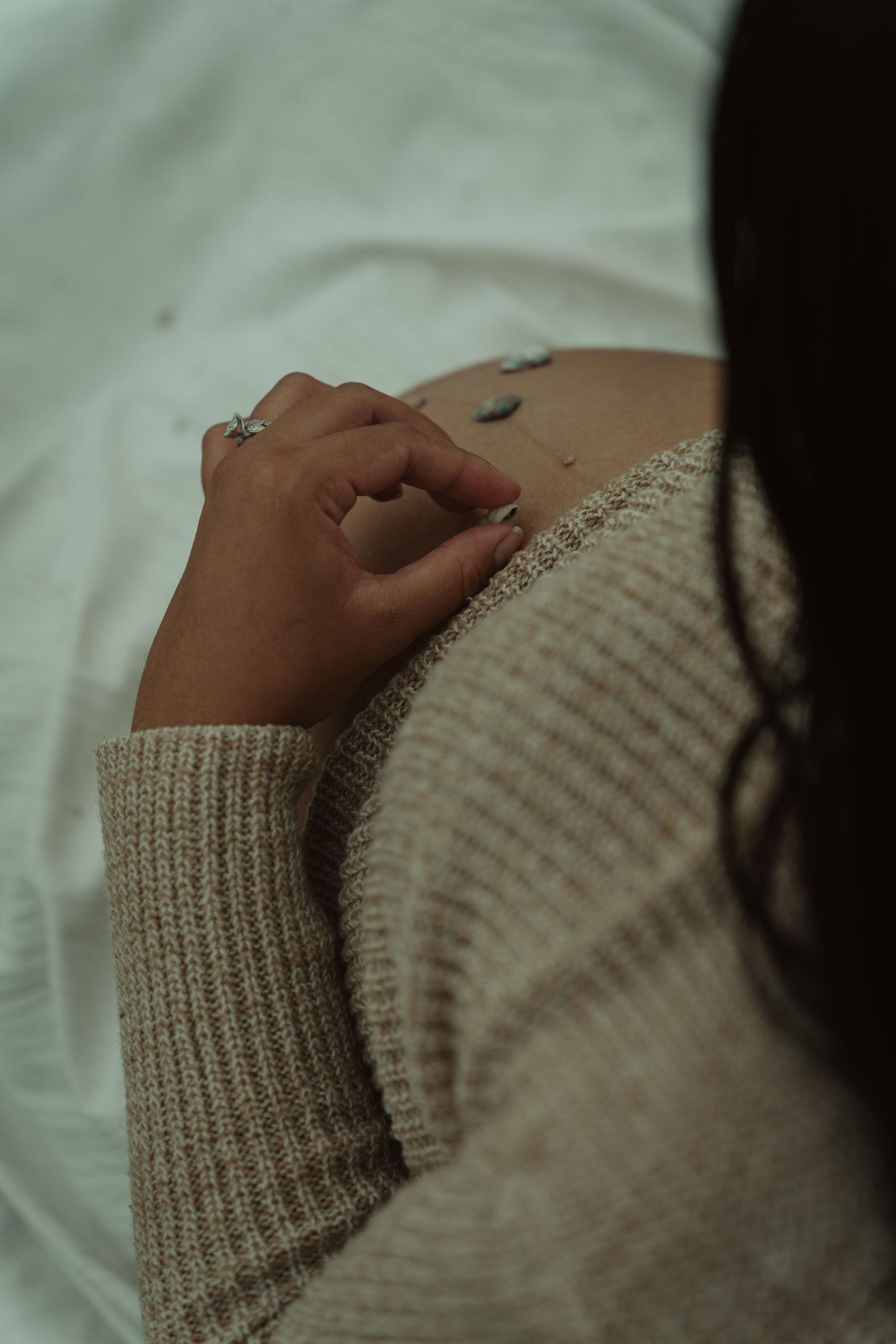 A close-up of a pregnant woman's hand with a ring resting on her bump in a beige sweater.