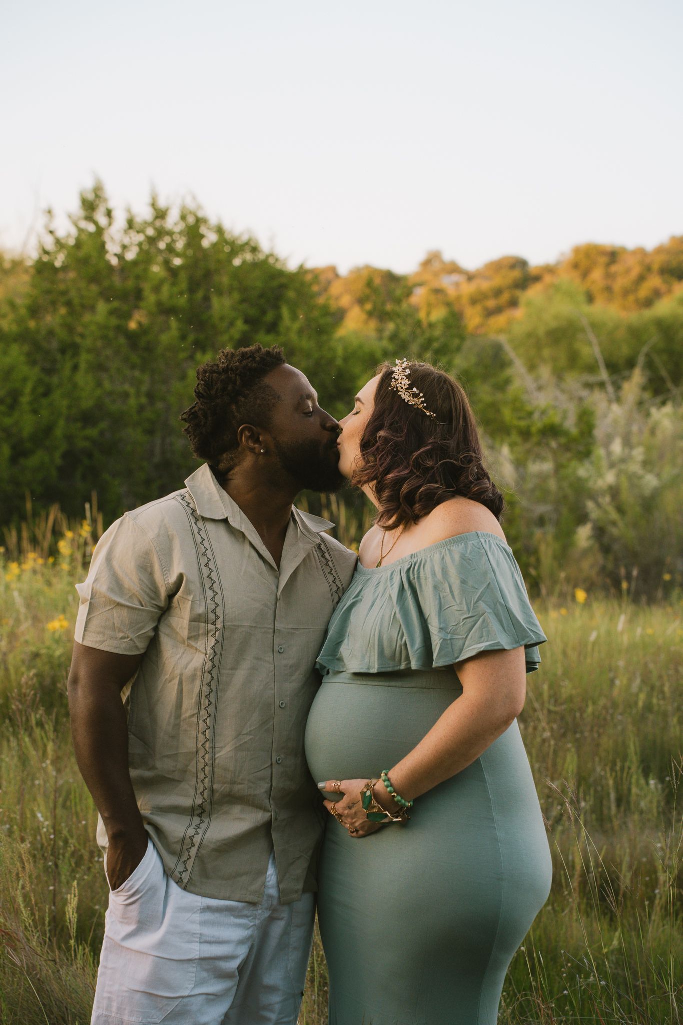 Interracial couple sharing a kiss outdoors during golden hour maternity photo session.