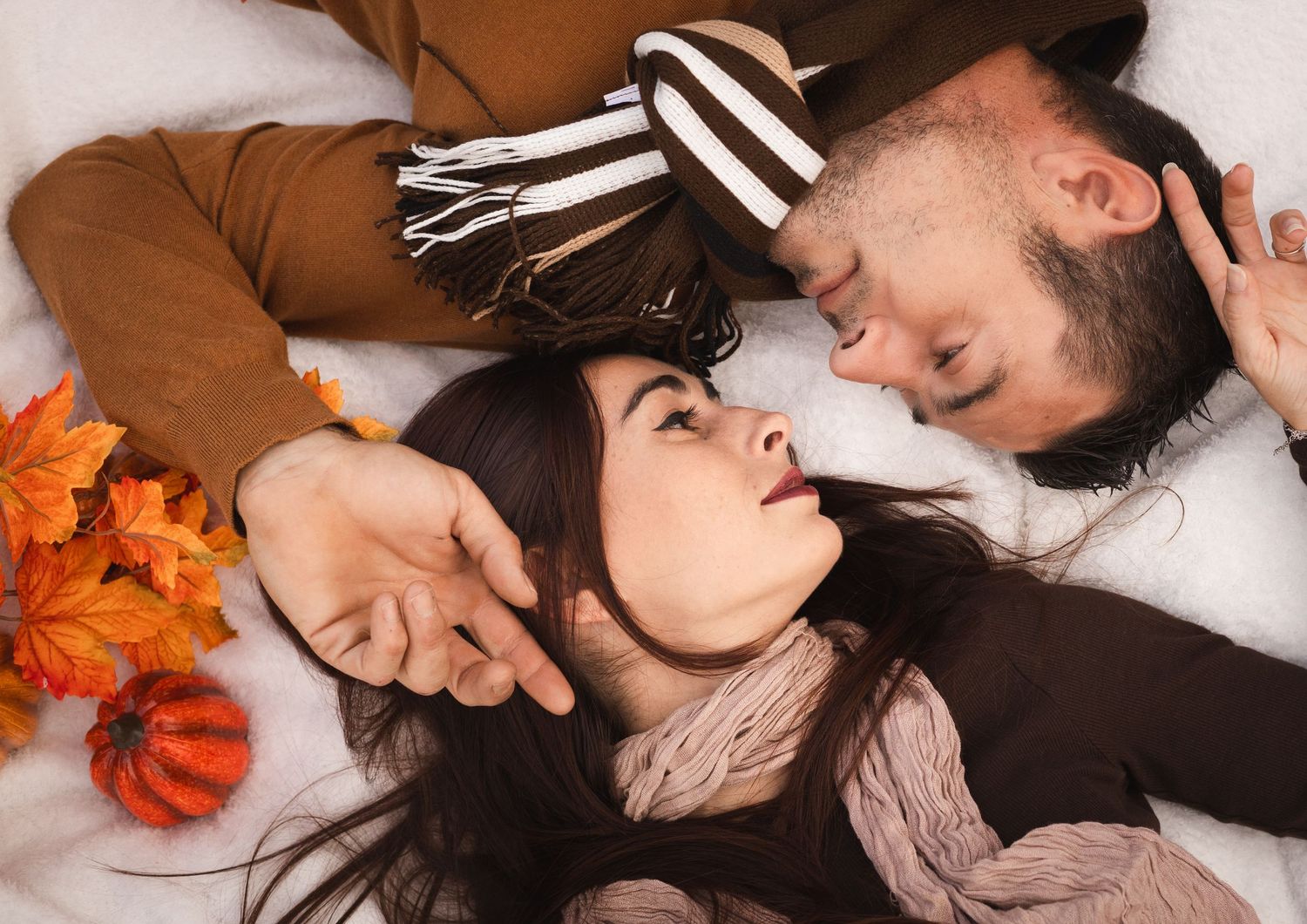 Deux personnes partagent un baiser romantique tout en étant allongées sur une surface blanche lors d'une séance photo de couple à Béziers.
