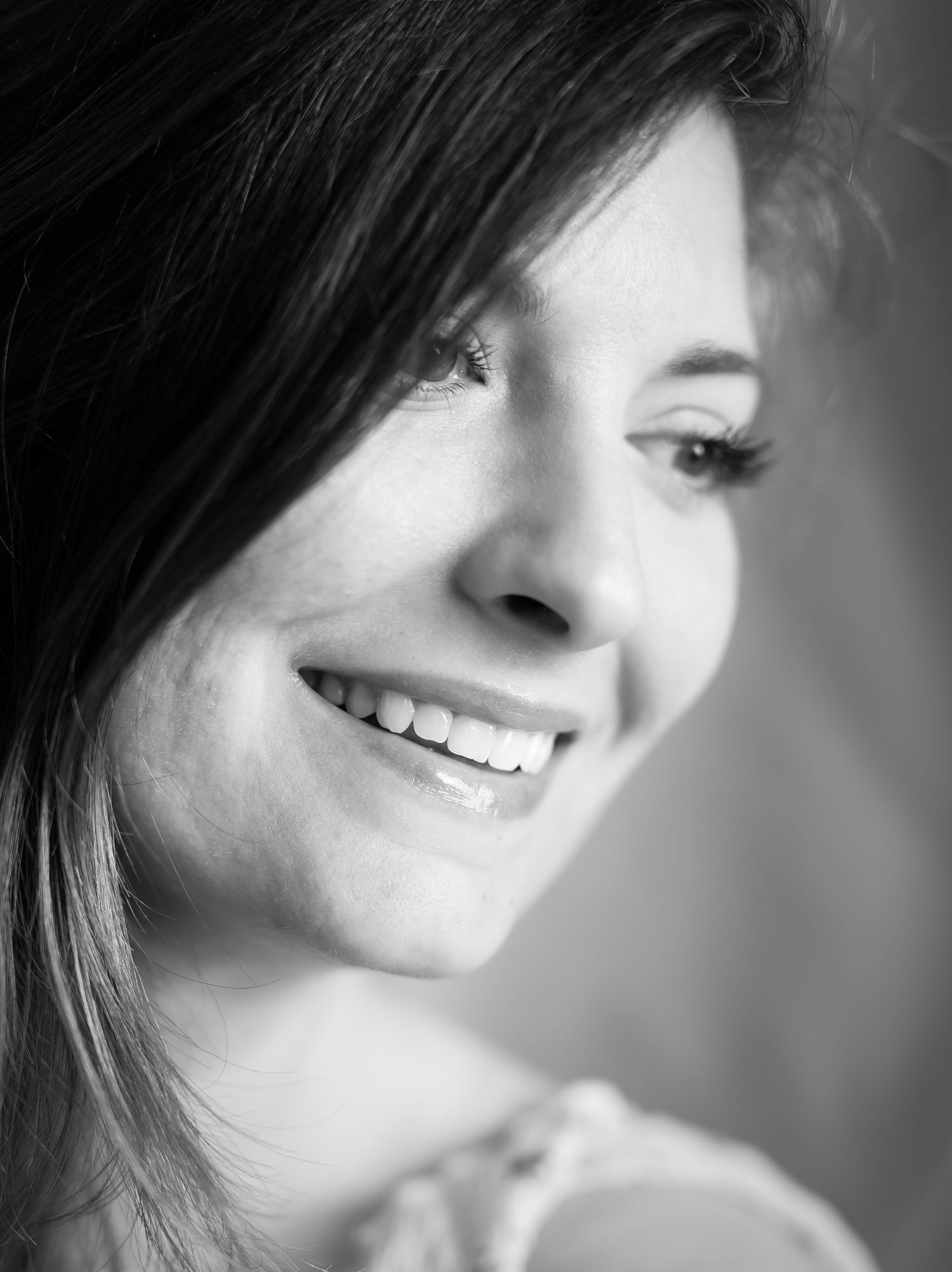 Portrait en noir et blanc d'une jeune femme souriante aux cheveux noirs, montrant la beauté et la joie naturelles.