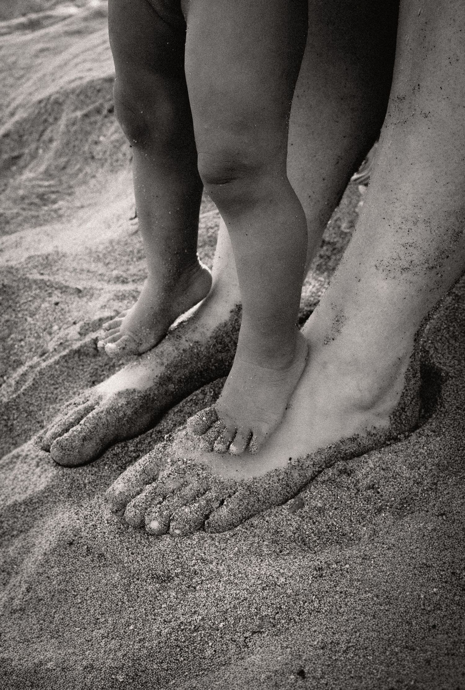 Photo en noir et blanc d'un adulte et d'un enfant pieds nus debout ensemble sur une plage de sable dans l'Hérault près de Béziers.