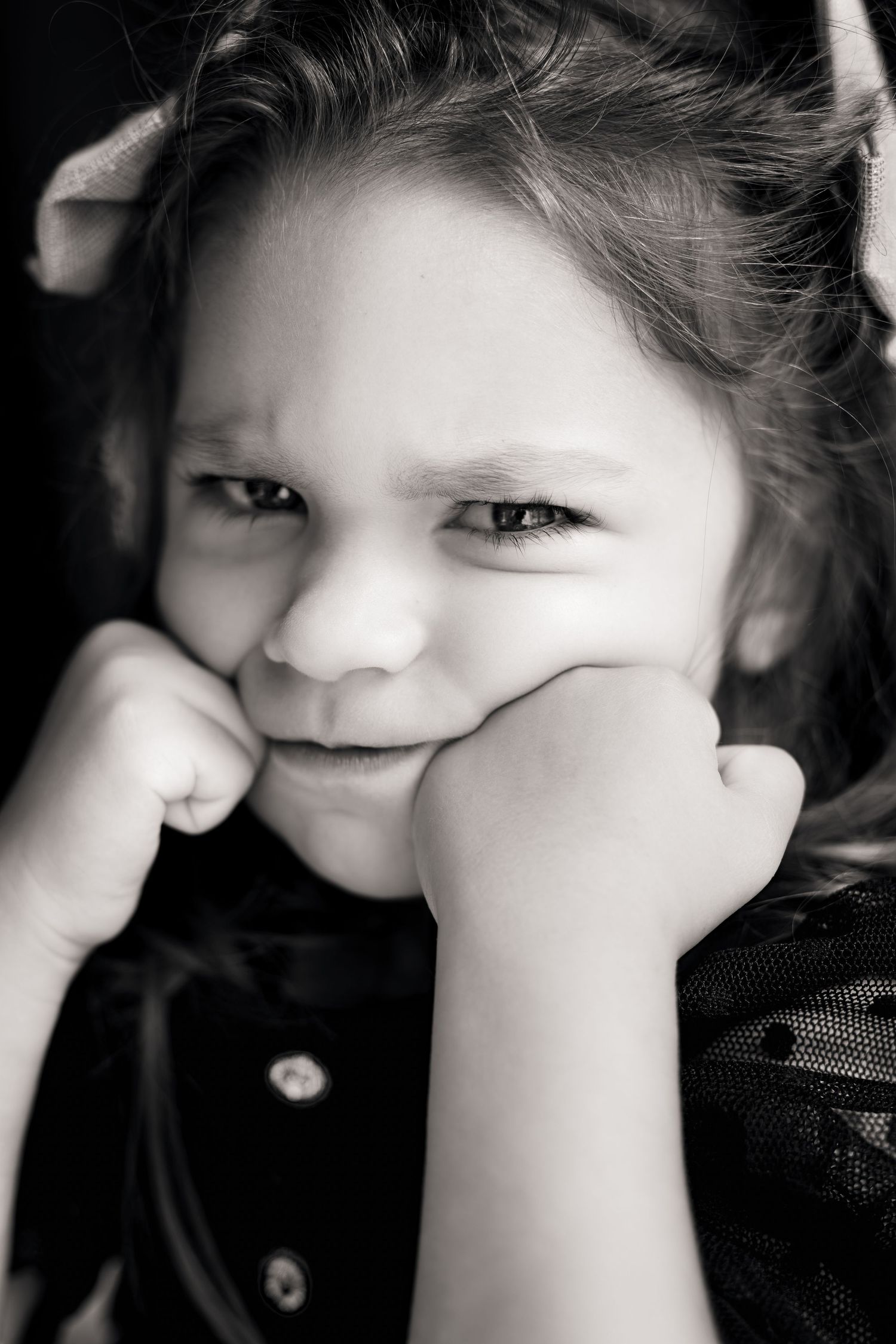 Black and white portrait of a young girl resting her chin on her fists with a pouty, brooding expression.