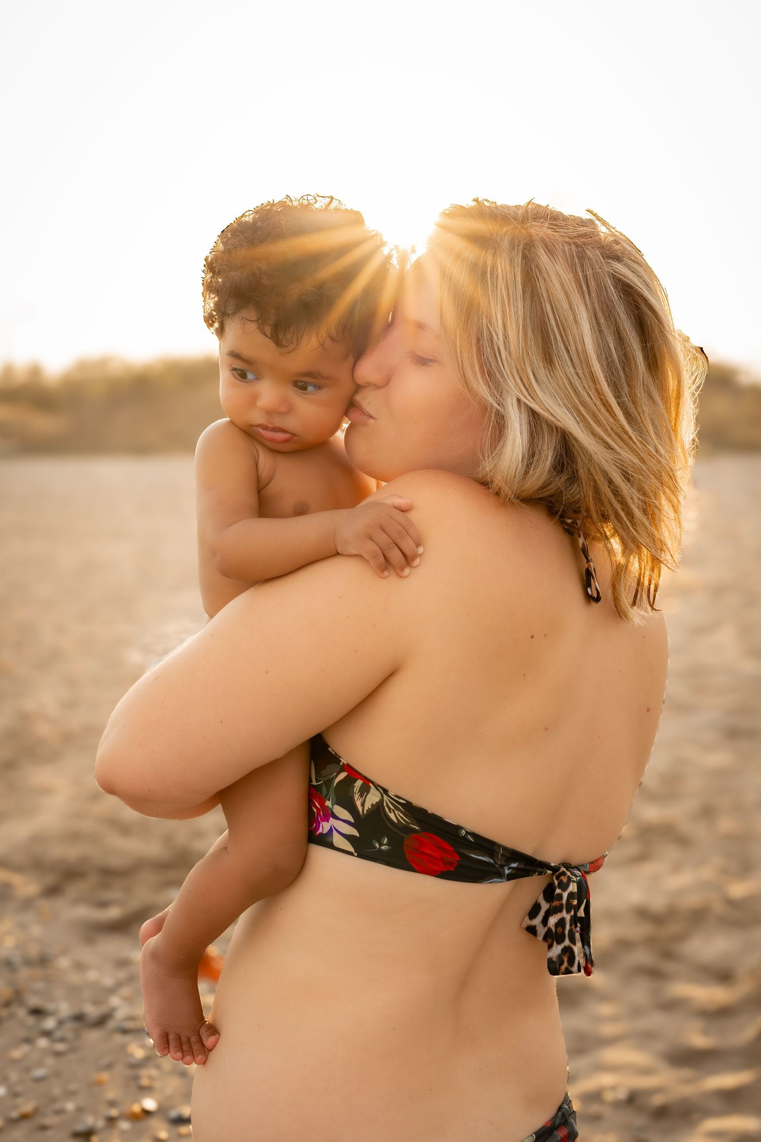 Une maman embrasse sa petite fille métisse lors d'une séance photo lifestyle mère et fille à portiragnes plage.