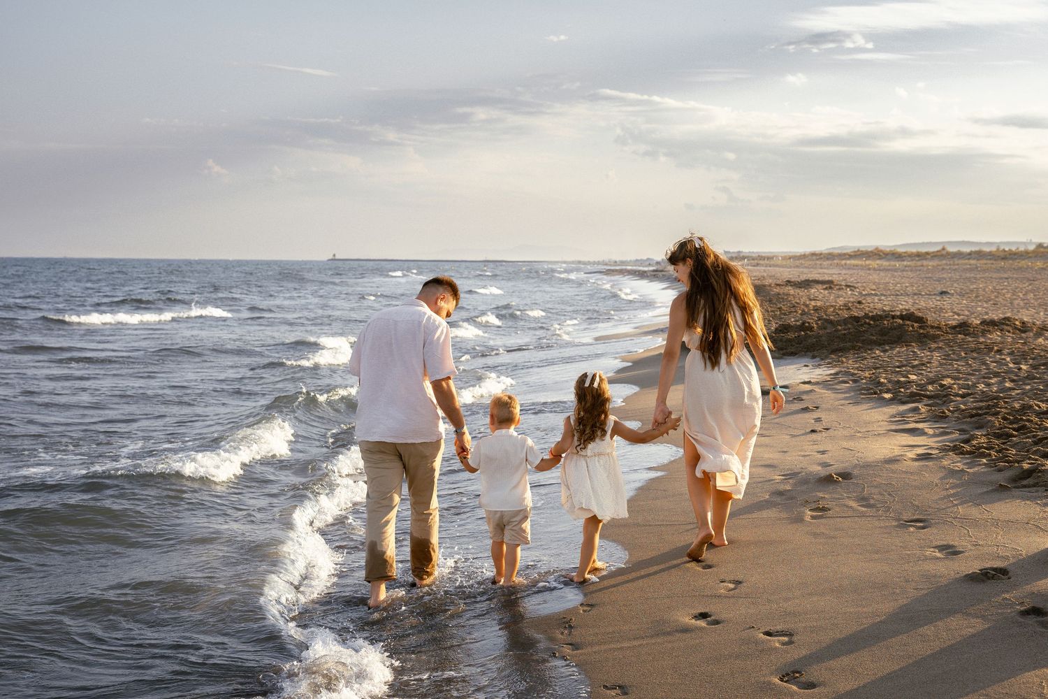 Photo famille de quatre personnes marchant main dans la main le long d'une plage de sable au coucher du soleil à Vendres plage