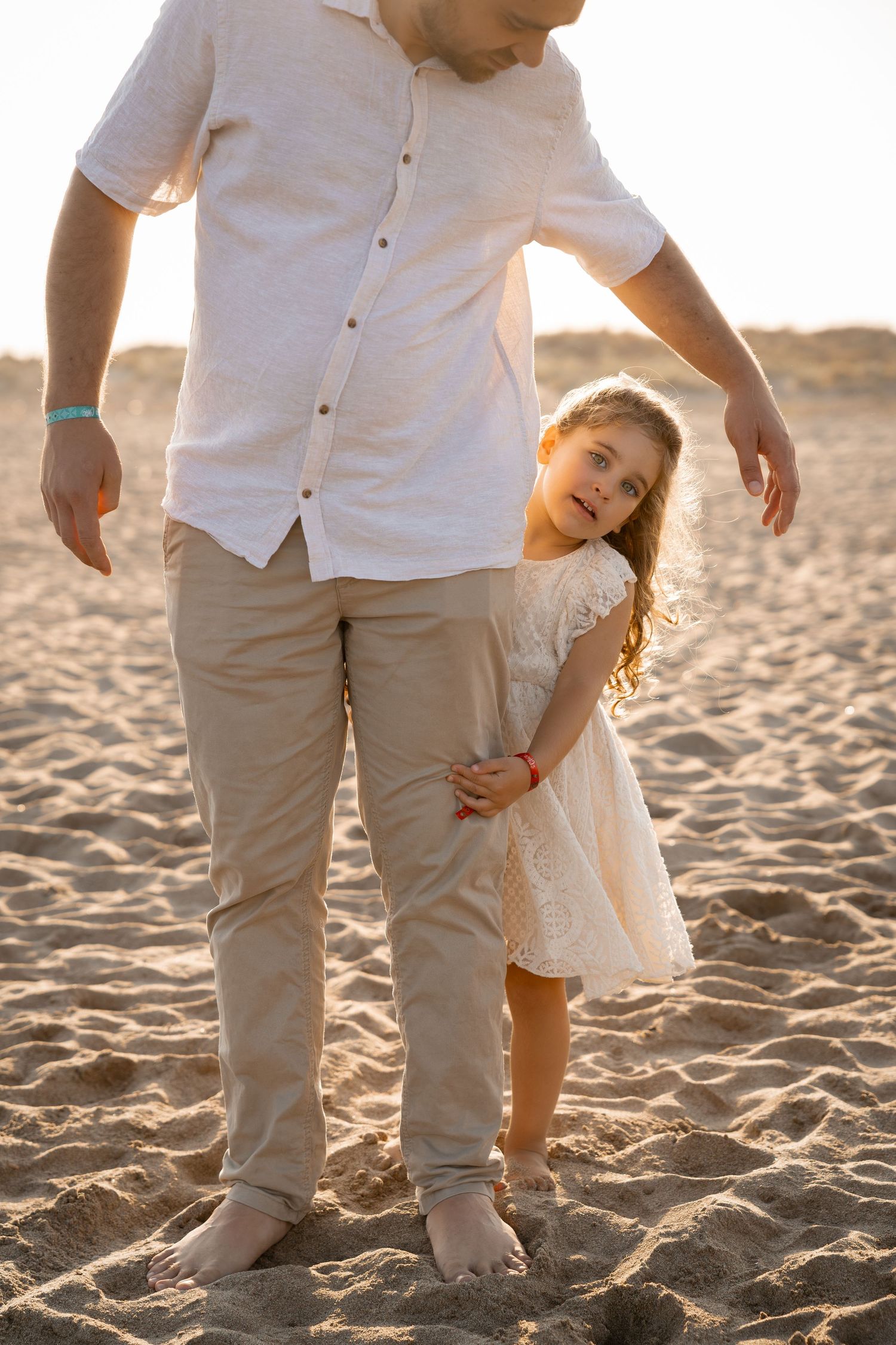 Une petite fille joue à cache-cache derrière son papa lors d'une séance photo en famille Vendres. Portrait d'un enfant au coucher de soleil.