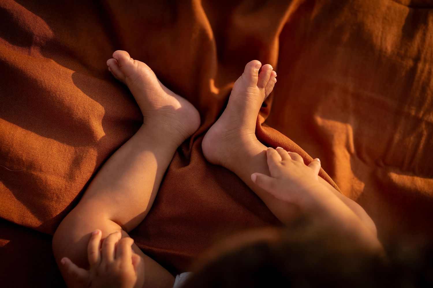 Gros plan des pieds de deux bébés reposant sur une douce couverture orange dans une lumière dorée chaude à Béziers.