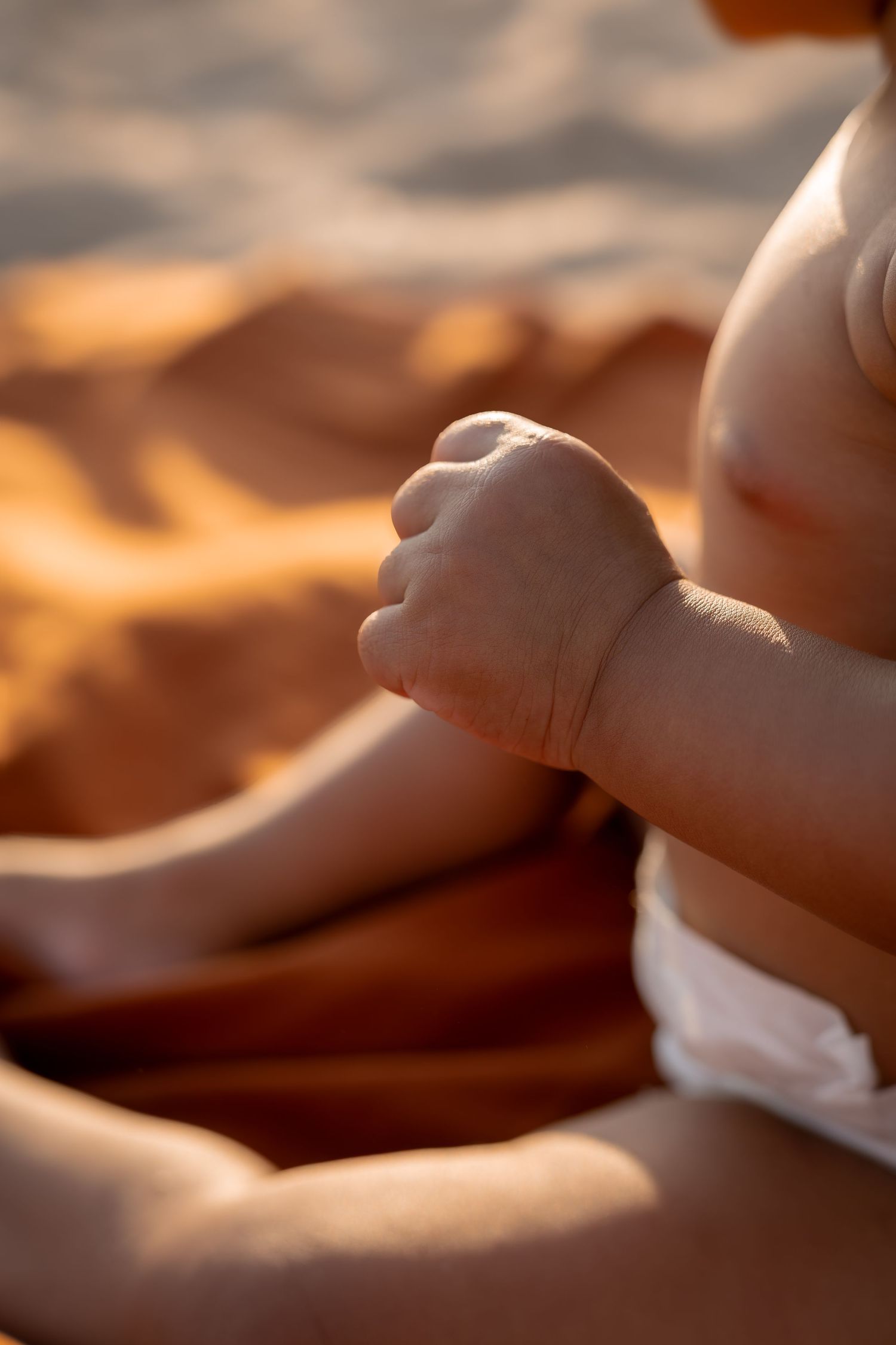 Photo détail petite main de bébé sur couverture terracotta à Portiragnes plage.