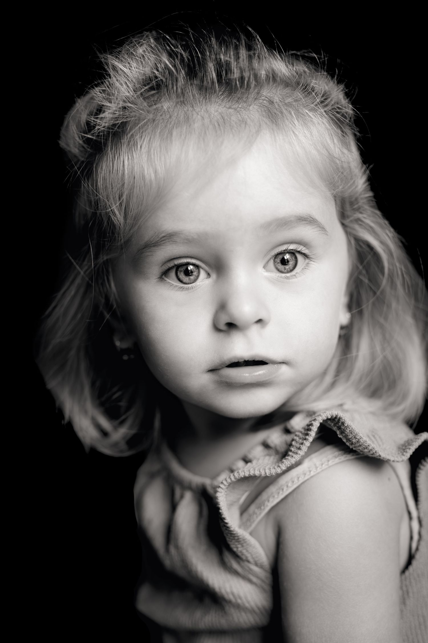Portrait d'enfant en noir et blanc. Photo en noir et blanc d'une petite fille blonde aux grands yeux bleus sur un fond sombre et noir.