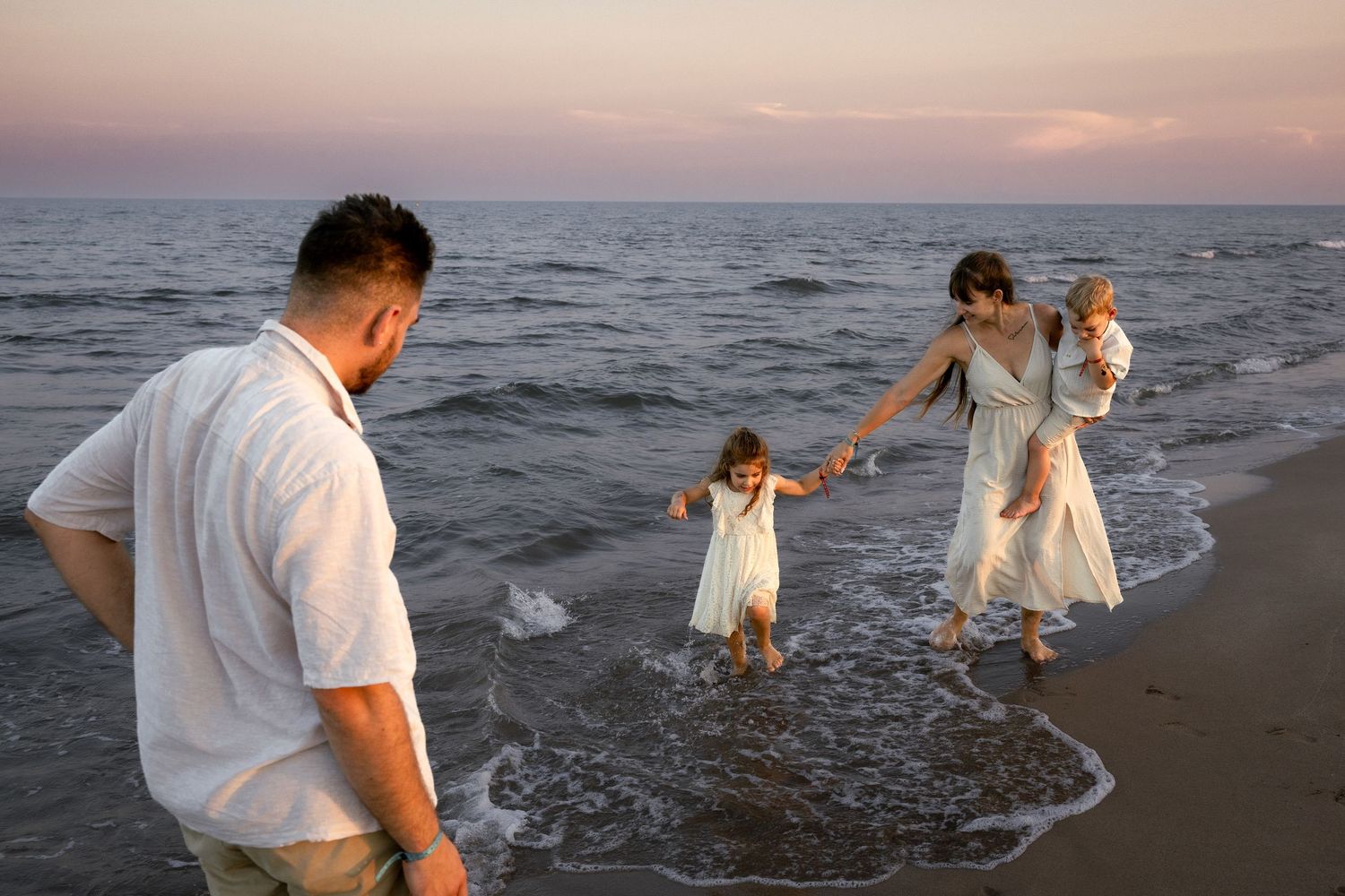 Famille profitant d'une promenade sur la plage au coucher du soleil, parents et deux jeunes enfants jouant dans les vagues de Valras plage.