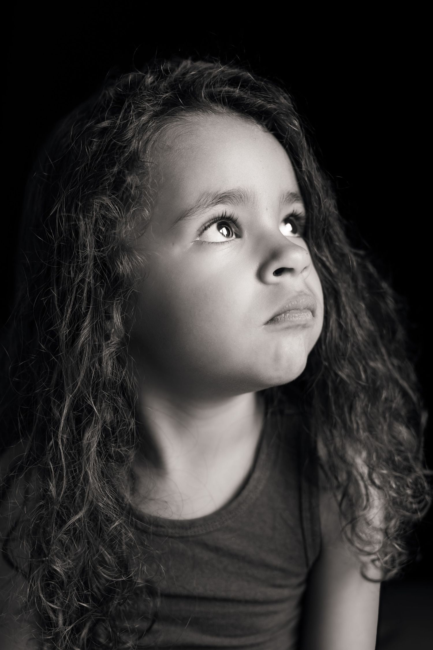 Portrait d'une petite fille métisse, moue boudeuse, cheveux longs et bouclés, photo en noir et blanc.