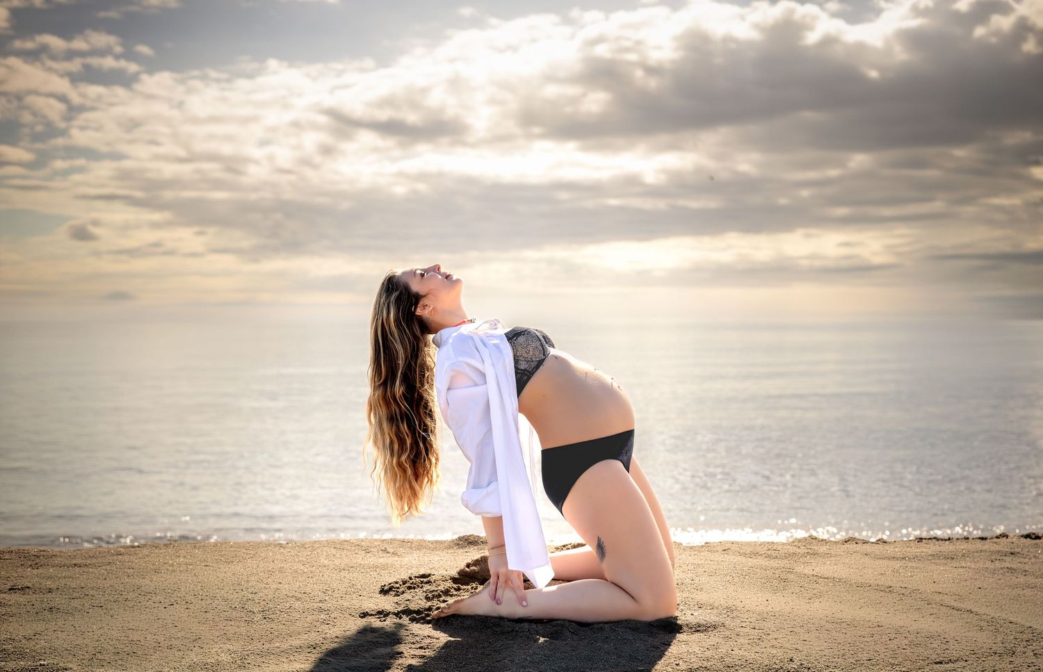 Séance photo grossesse artistique. Une femme enceinte pose devant un ciel spectaculaire lors d'une séance photo grossesse à Serignan plage.
