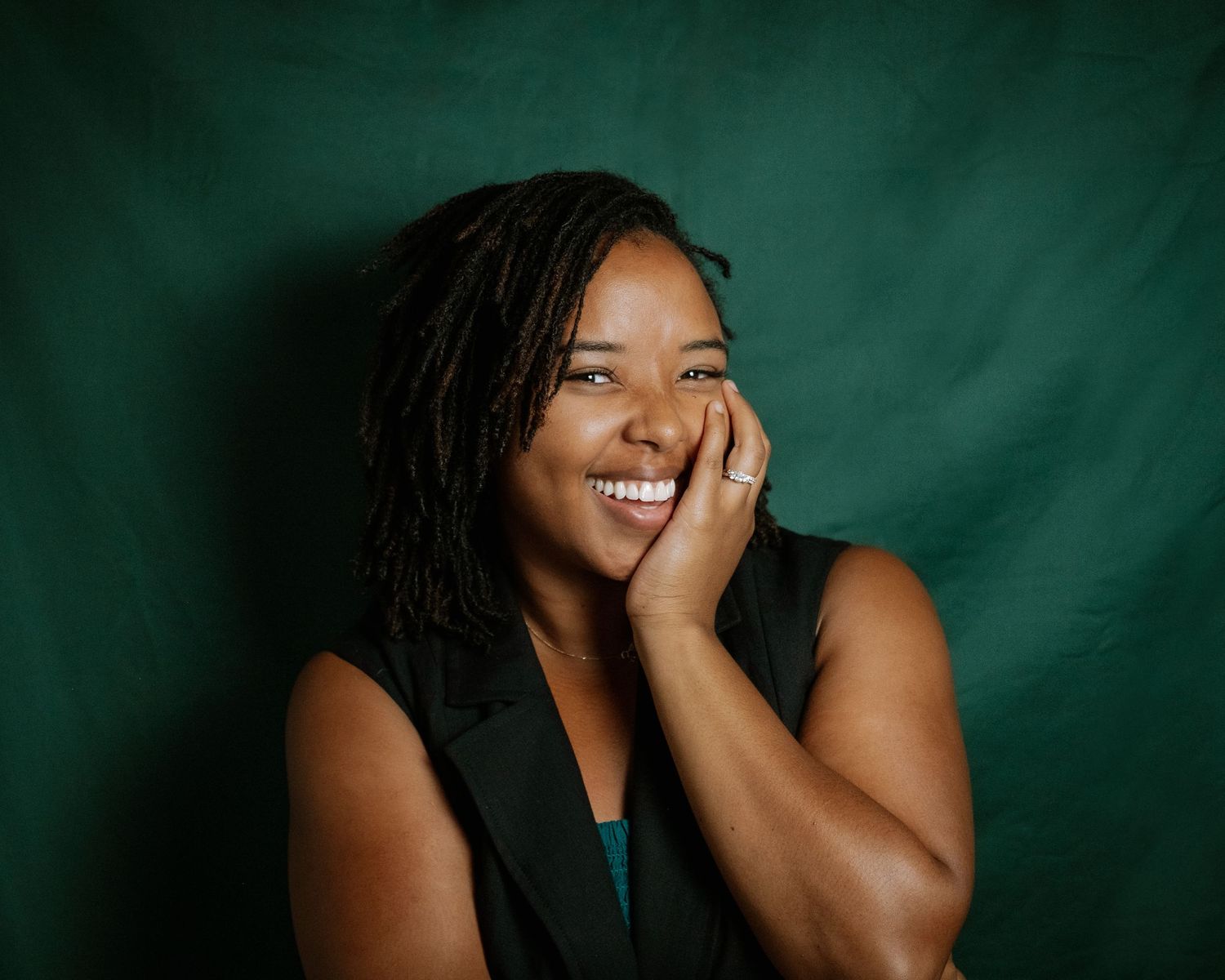 African American Professional portrait photographer against emerald green backdrop showing joyful expression and casual black top.
