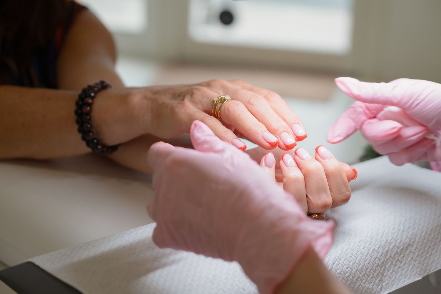 Close-up view of hands receiving professional manicure treatment at nail salon with pink polish application.