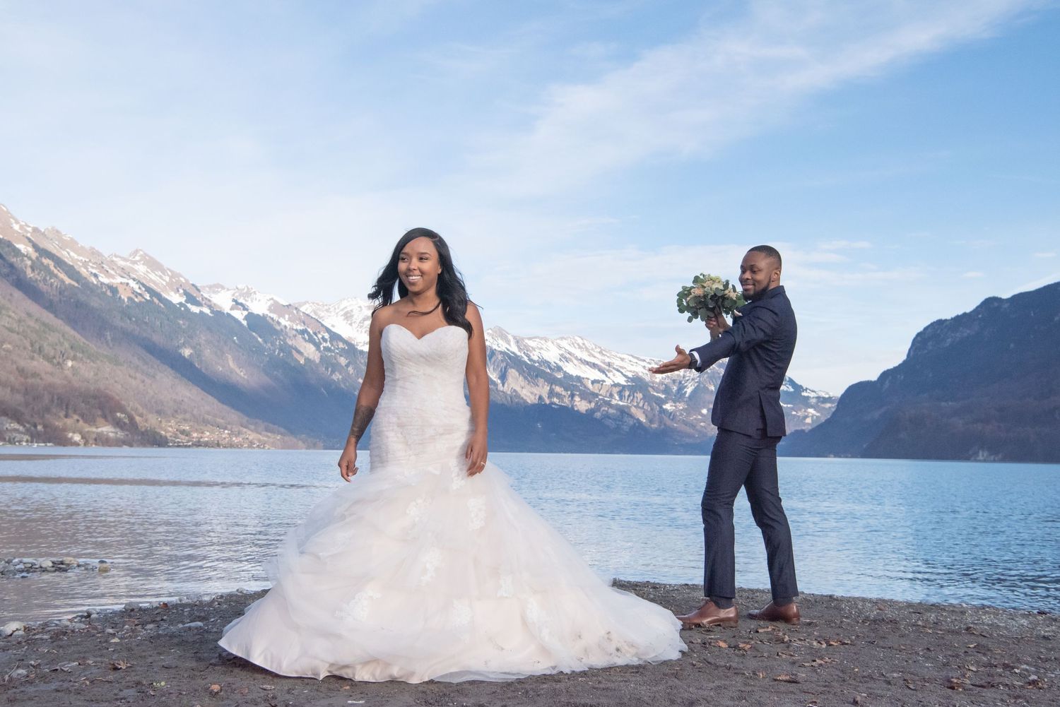 Wedding photography scene at mountain lake with snow-capped peaks in background.