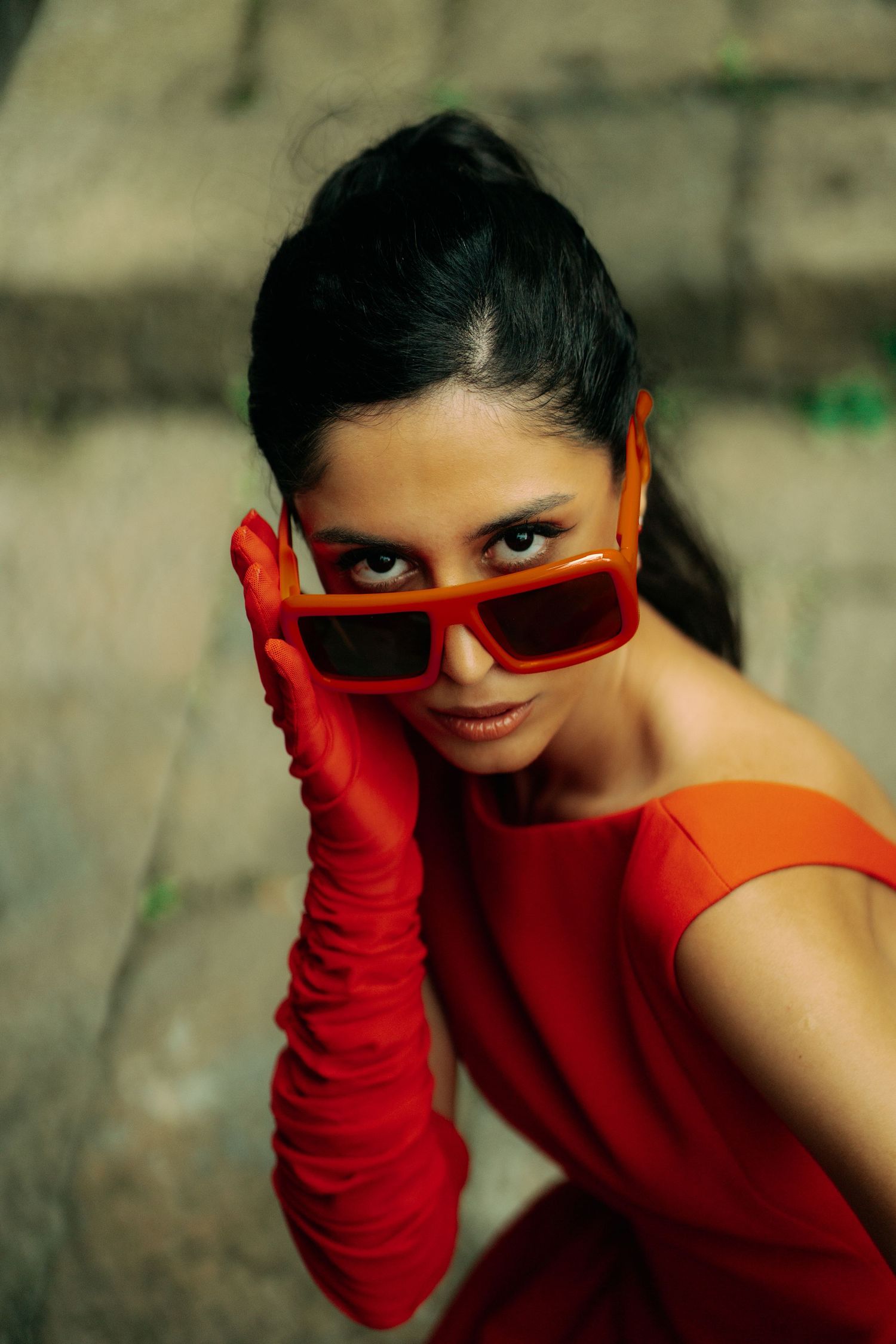 Fashion portrait featuring red gloves and sunglasses against a concrete background.