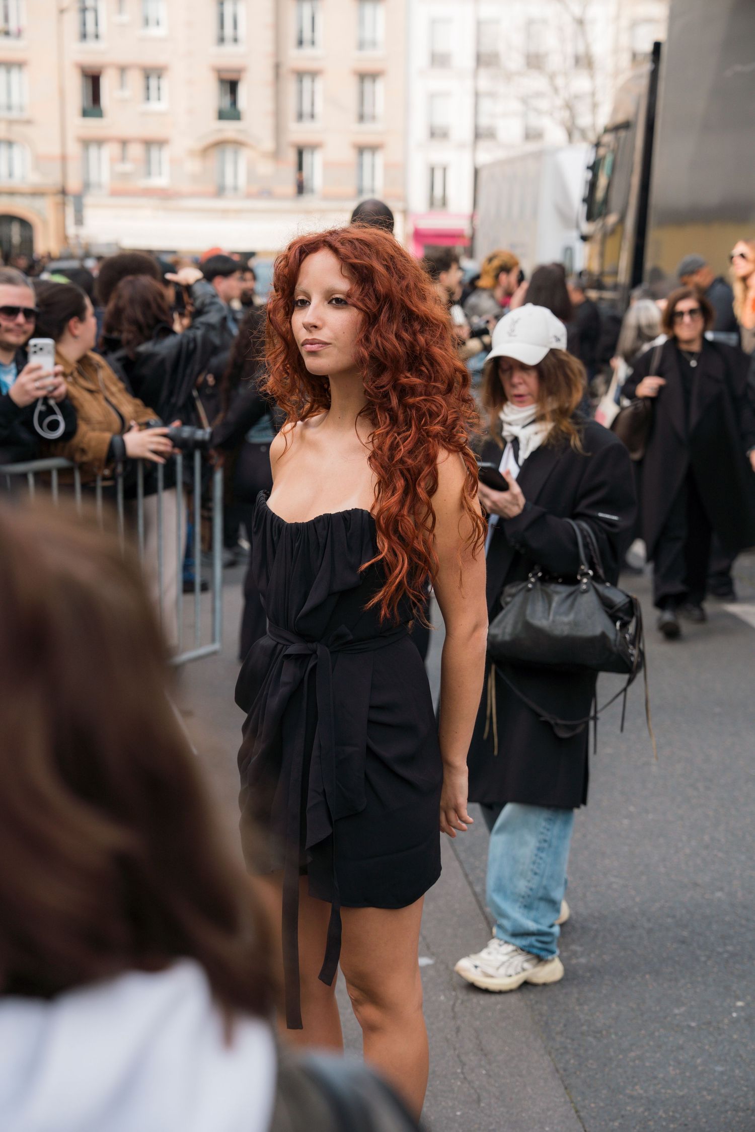 A person with flowing red curly hair dances energetically in an outdoor crowd setting.