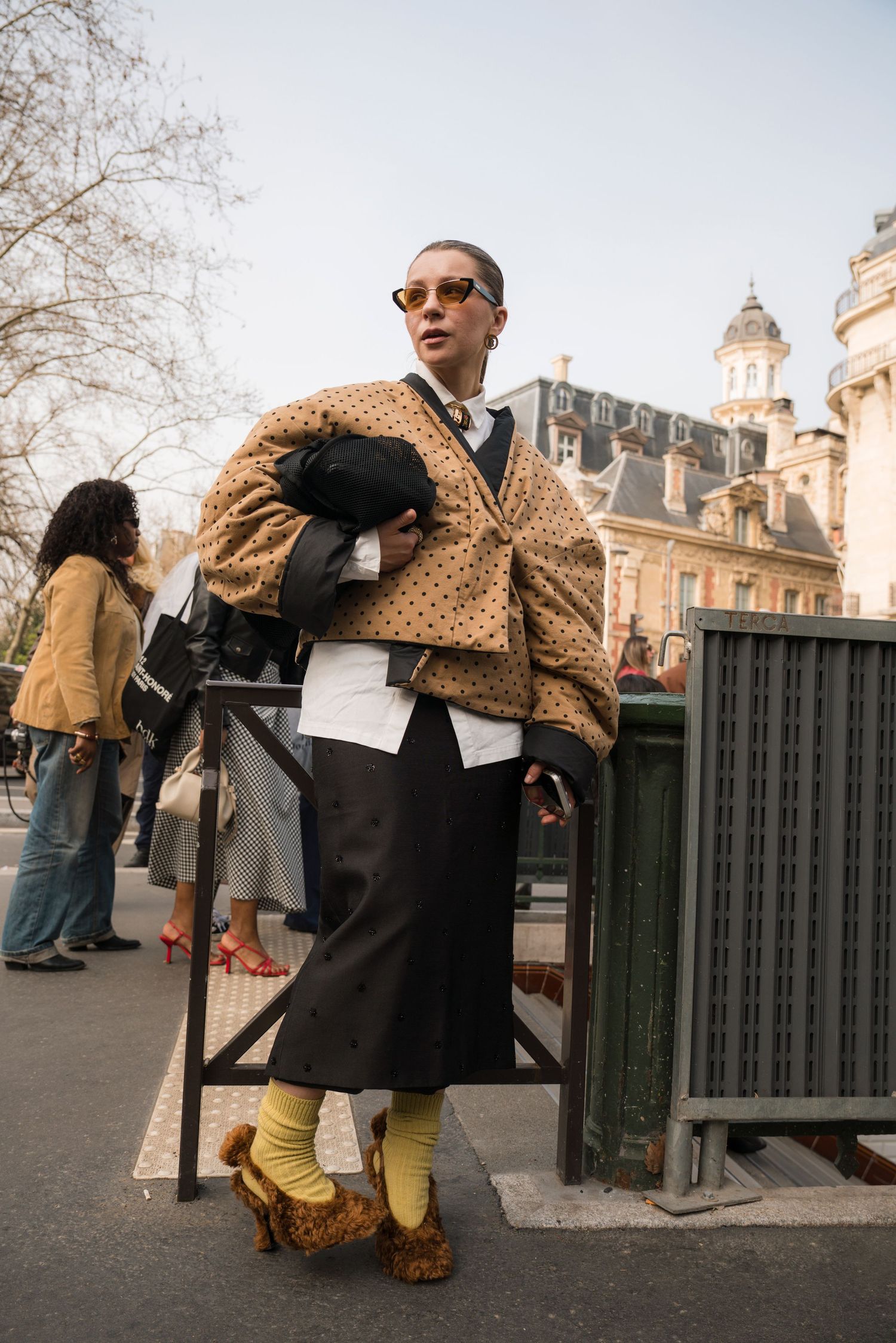 A series of fashion photos showing details of a polka dot coat and black dress against an urban backdrop.