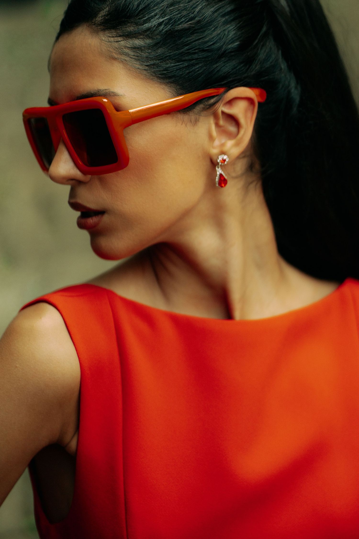 Fashion portrait showing red sunglasses and matching red top against neutral background in artistic composition.