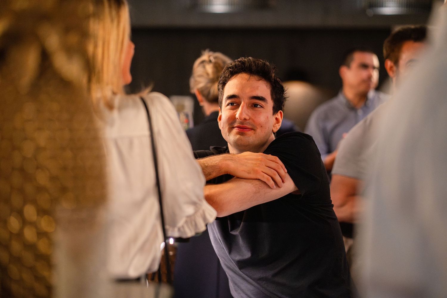 Group of people having lively conversations at a social gathering in a dimly lit indoor setting.