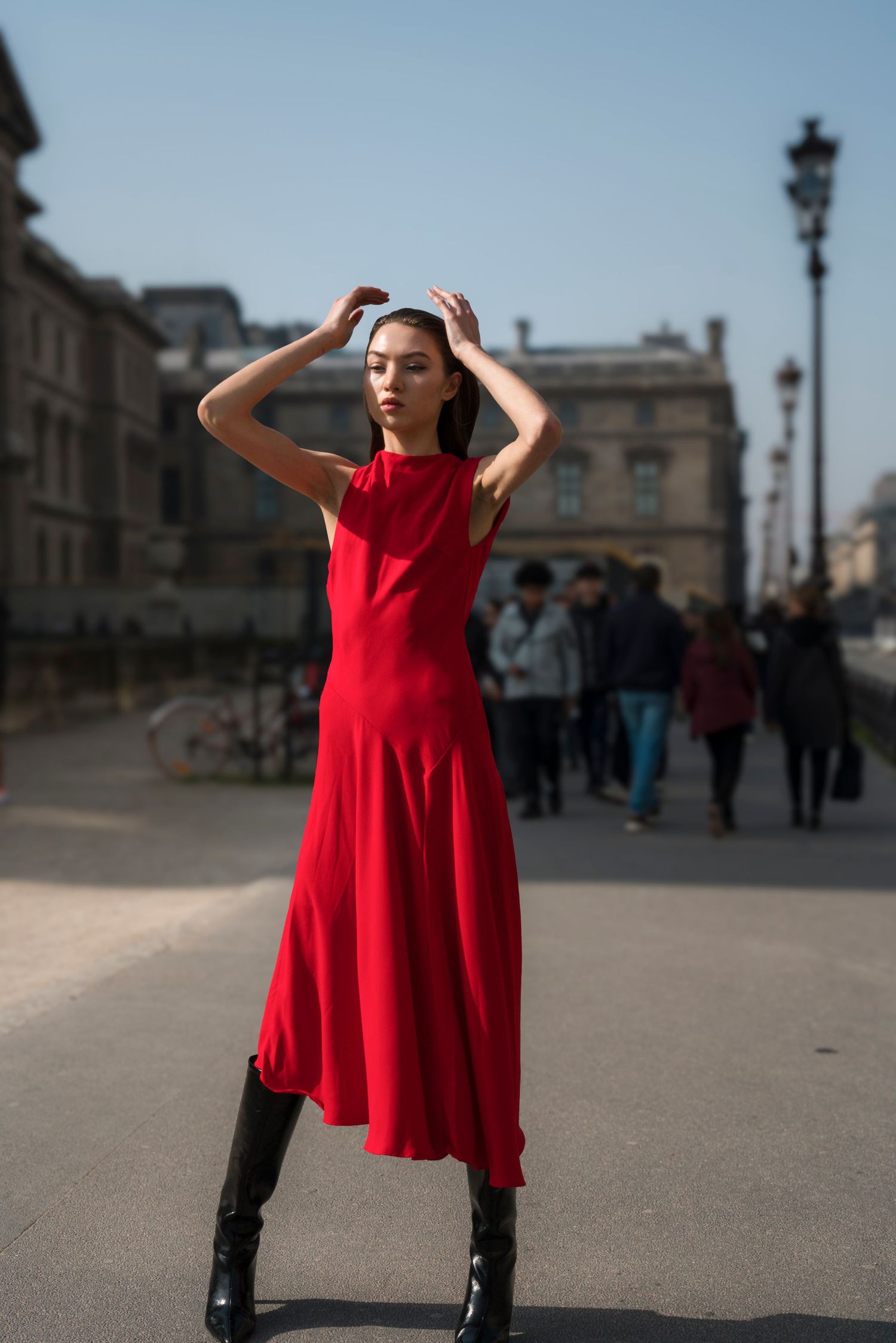 A figure in a flowing red dress and black boots poses dramatically on a city street in multiple sequential shots.