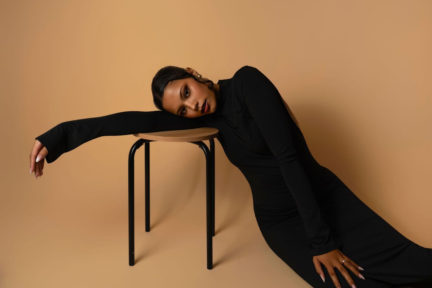 A dancer in black clothing performs a dynamic sequence of contemporary dance movements against a beige backdrop.