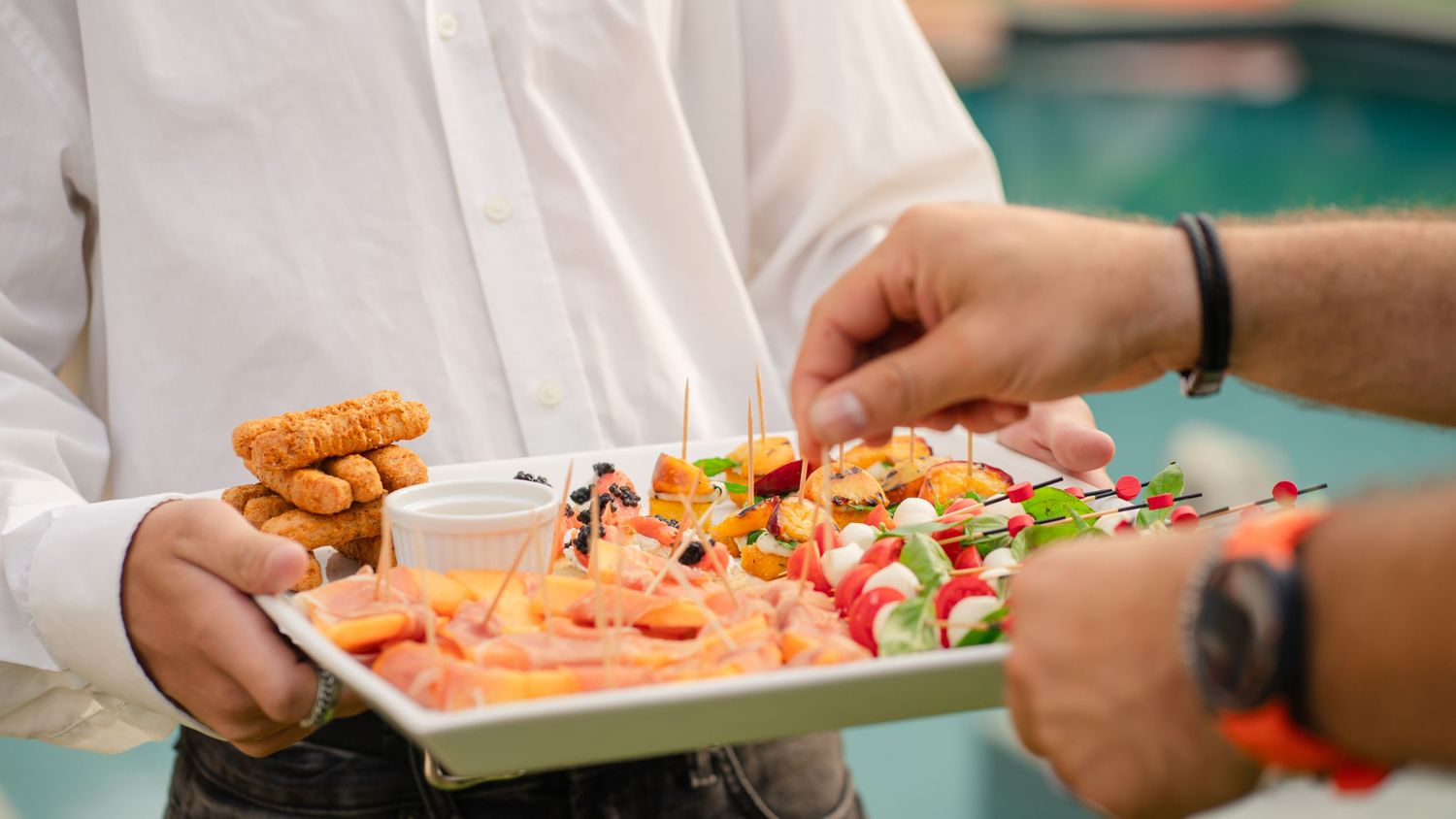 A platter of fresh sushi rolls and appetizers being served at a restaurant with hands visible in the frame.