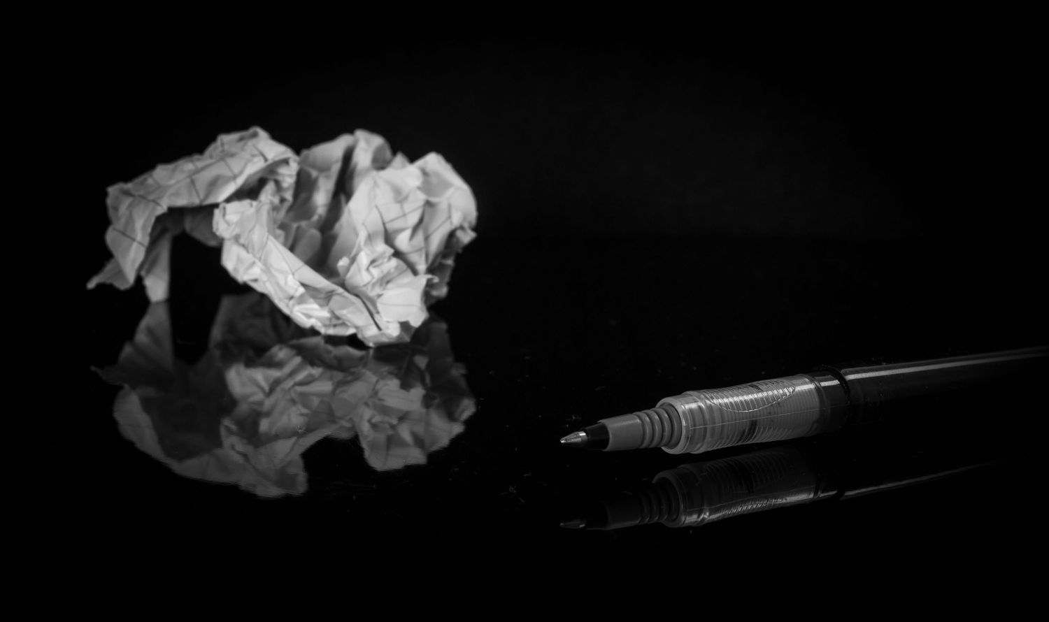 Black and white photo of a crumpled paper and pen on reflective surface.