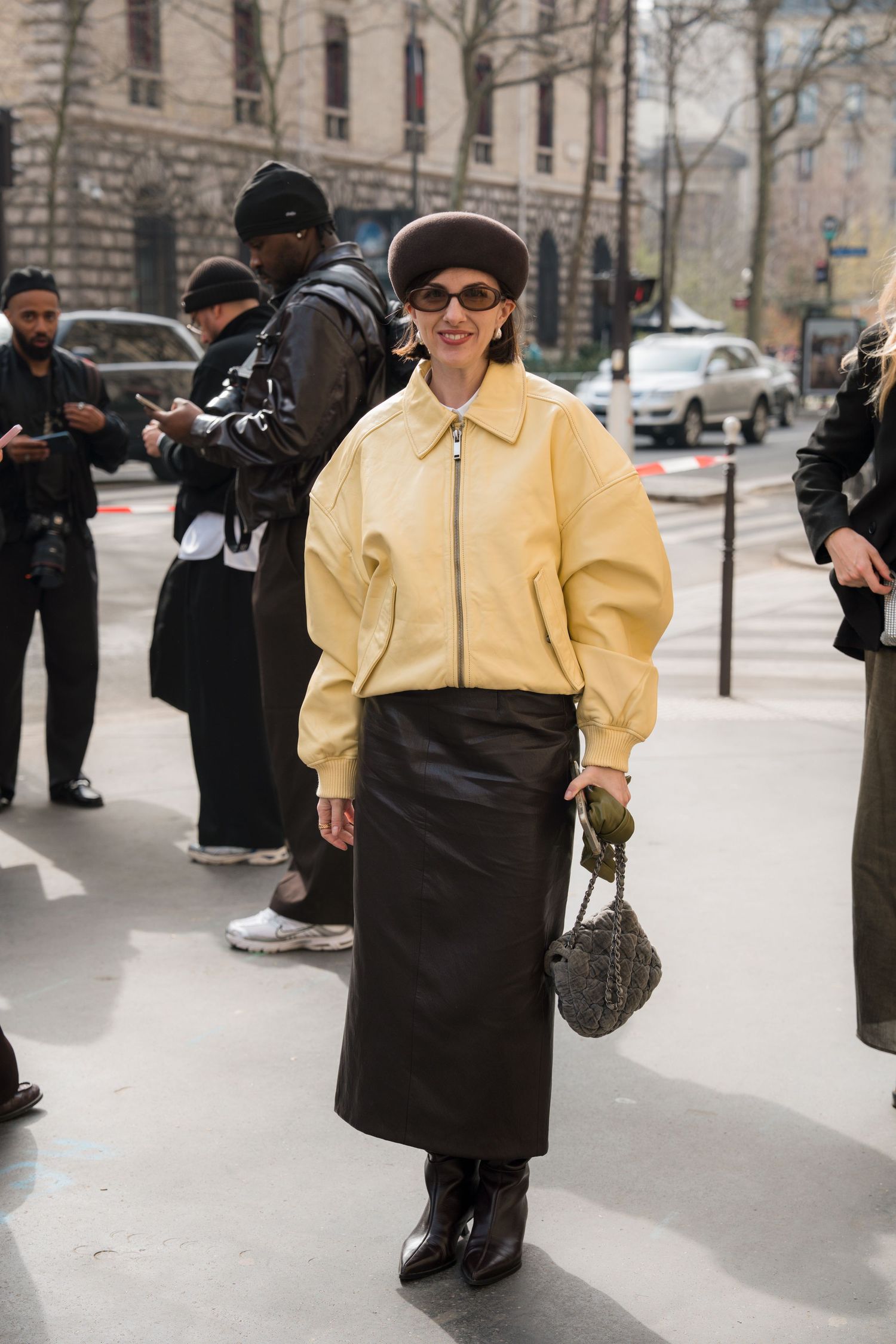 Person in yellow puff-sleeve top and black skirt walking down urban street while photographers capture the moment.