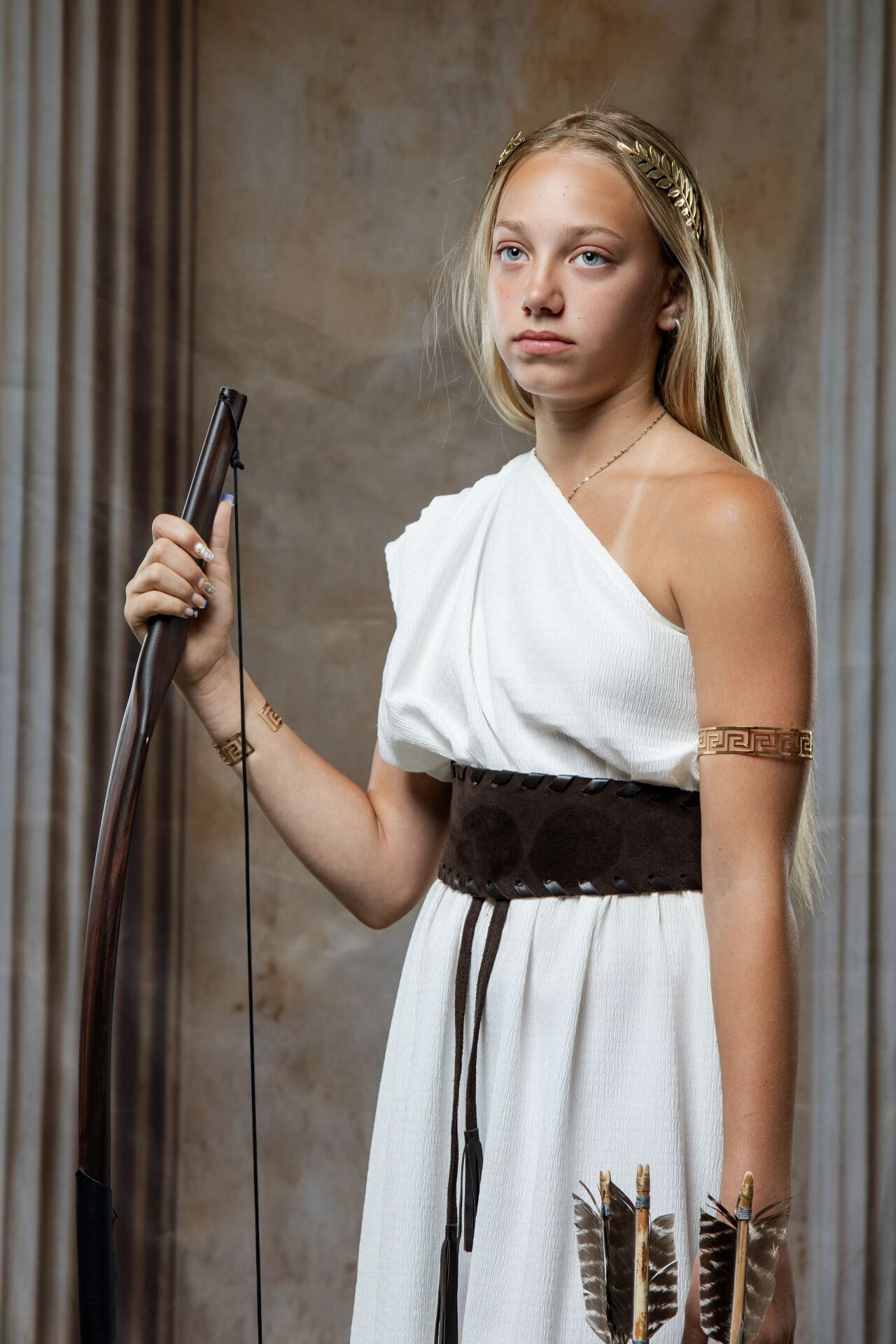 Artemis  white Greek costume holding a bow with arrow quiver, wearing gold armband and leather belt.