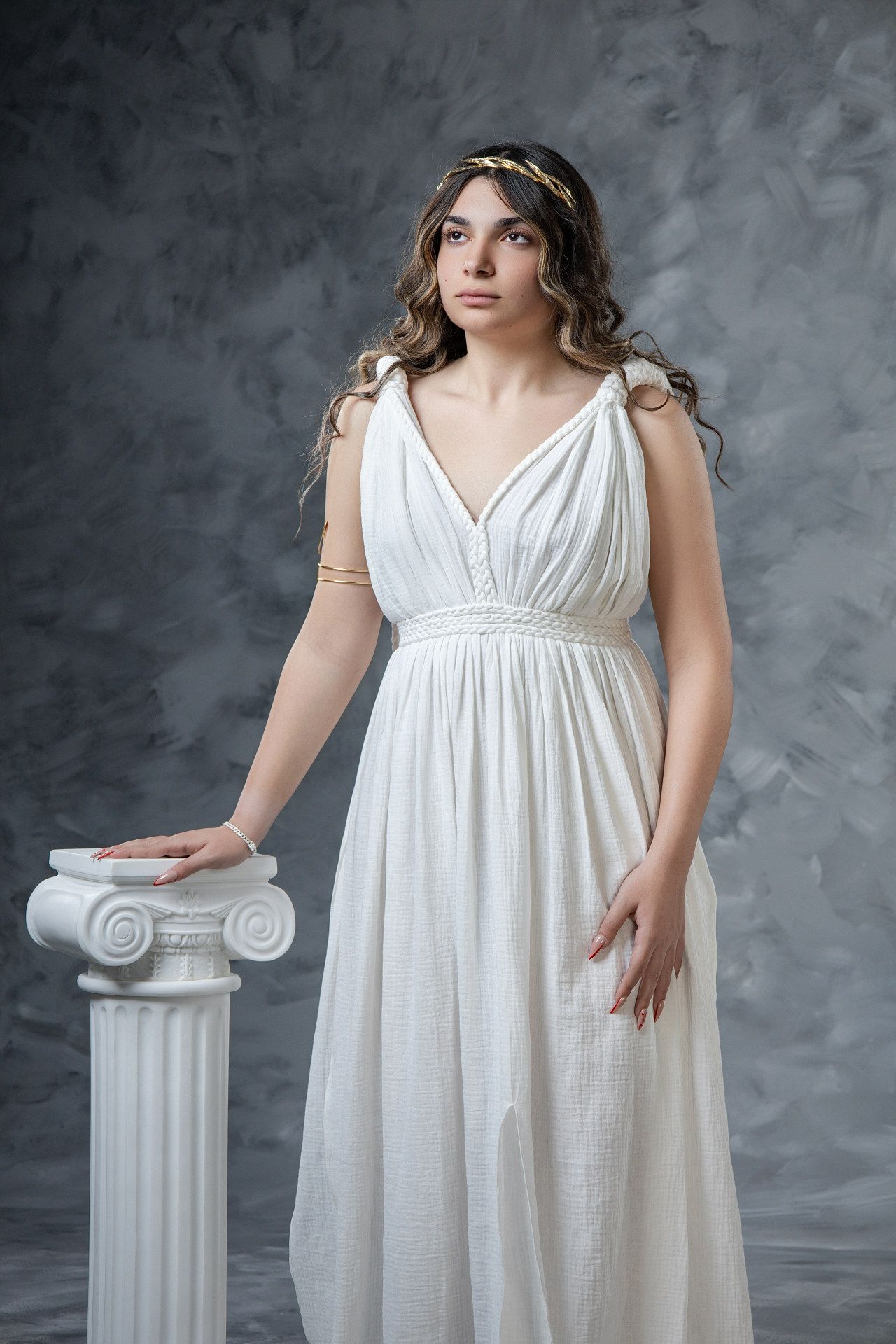 Ancient Greek woman portrait in flowing white empire waist dress beside classical white column, studio Hellenic-style photography by GreekCl