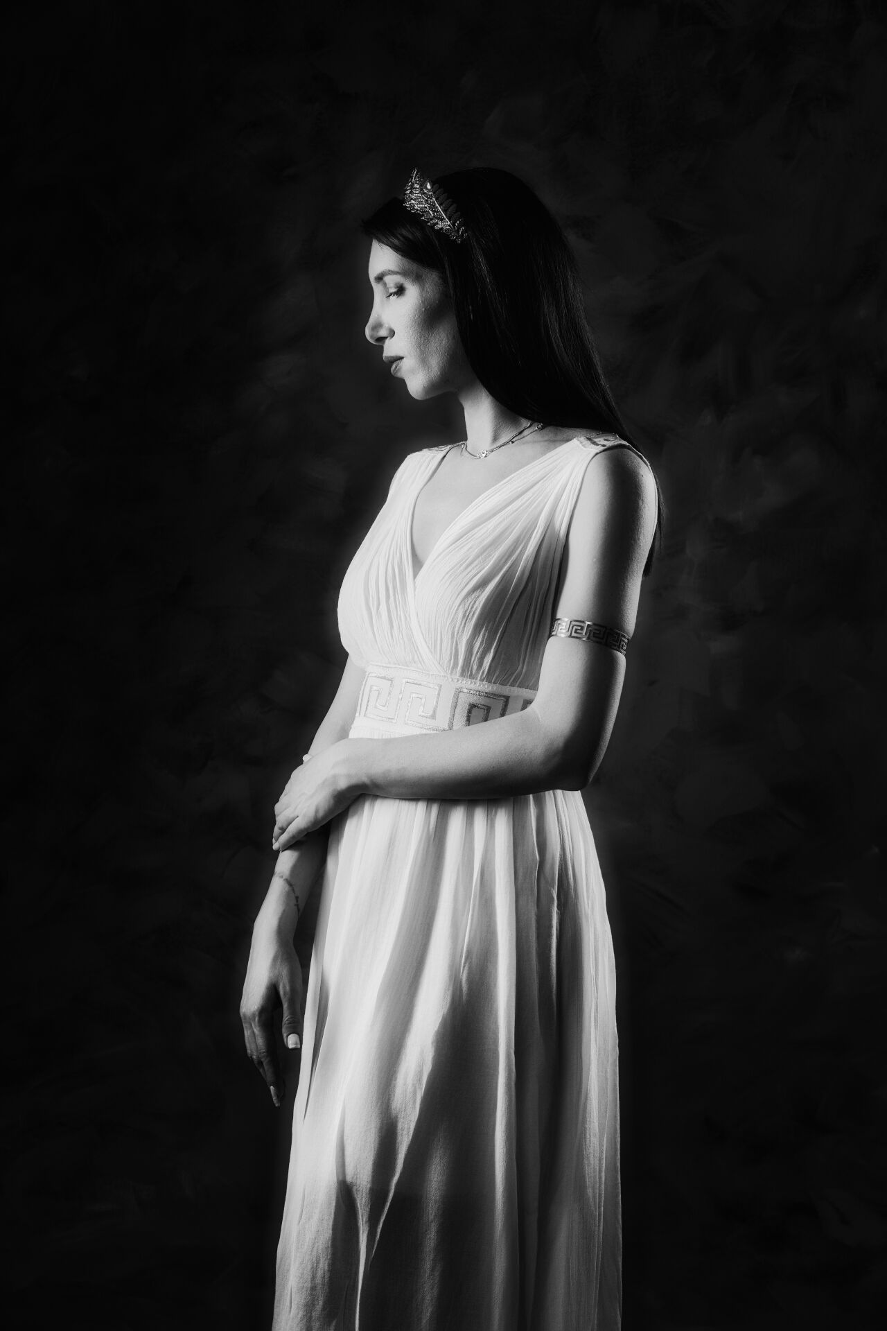 Αrtistic portrait showing a woman in a flowing white toga against a dark background.