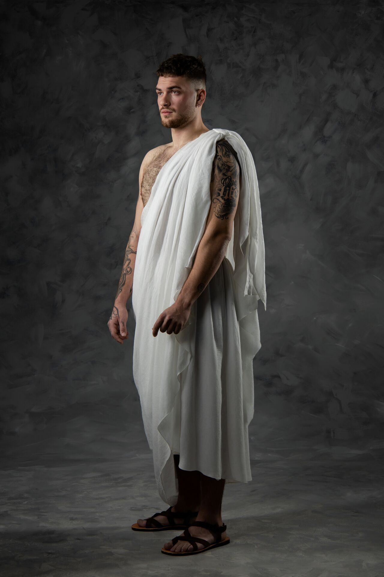 A figure in a flowing white toga-style garment and sandals stands against a dark gray backdrop in various poses.