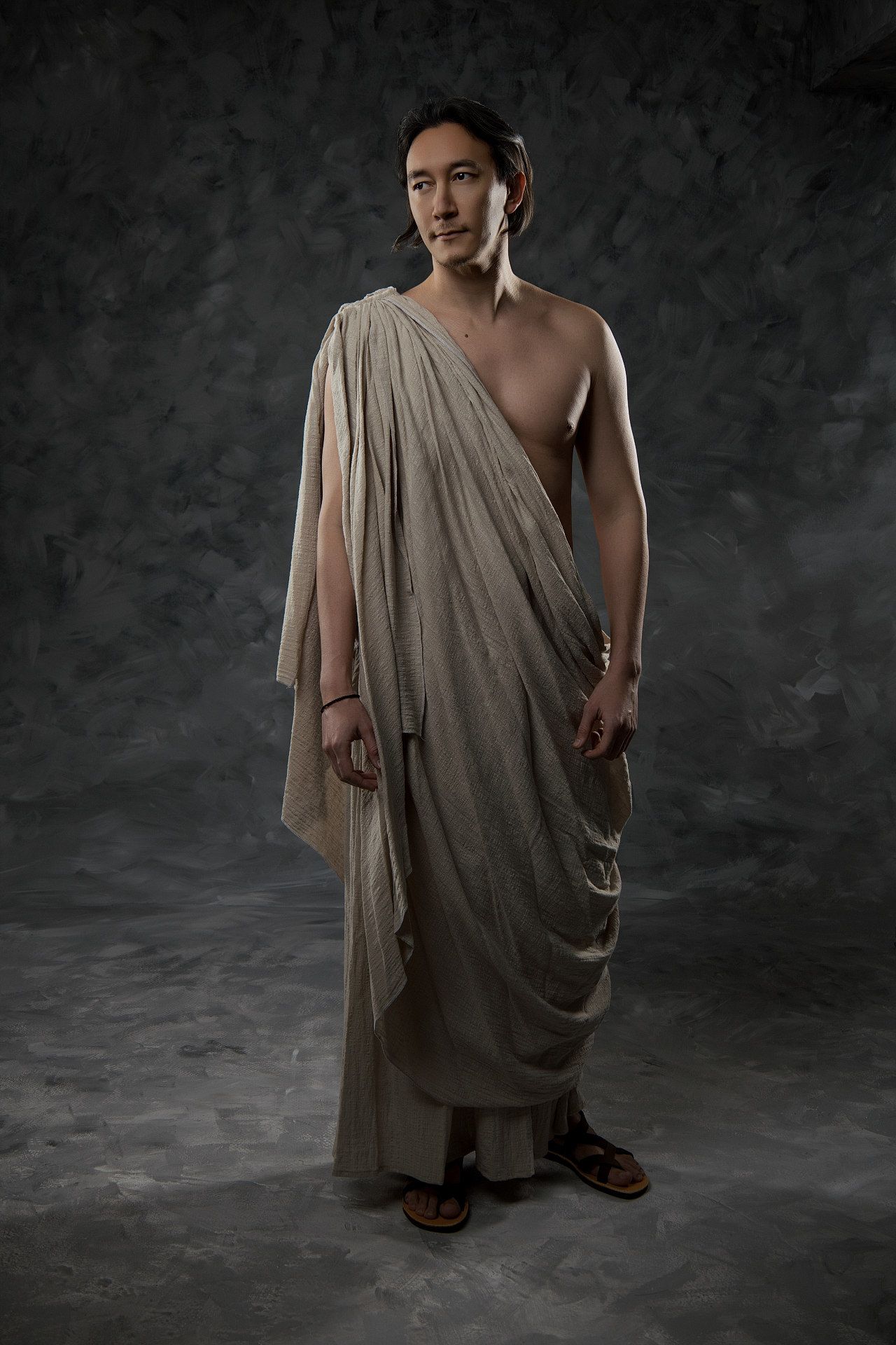 Ancient Greek toga-style portrait of figure in draped beige garment against dark background, dramatic Hellenic-style photoshoot GreekClick