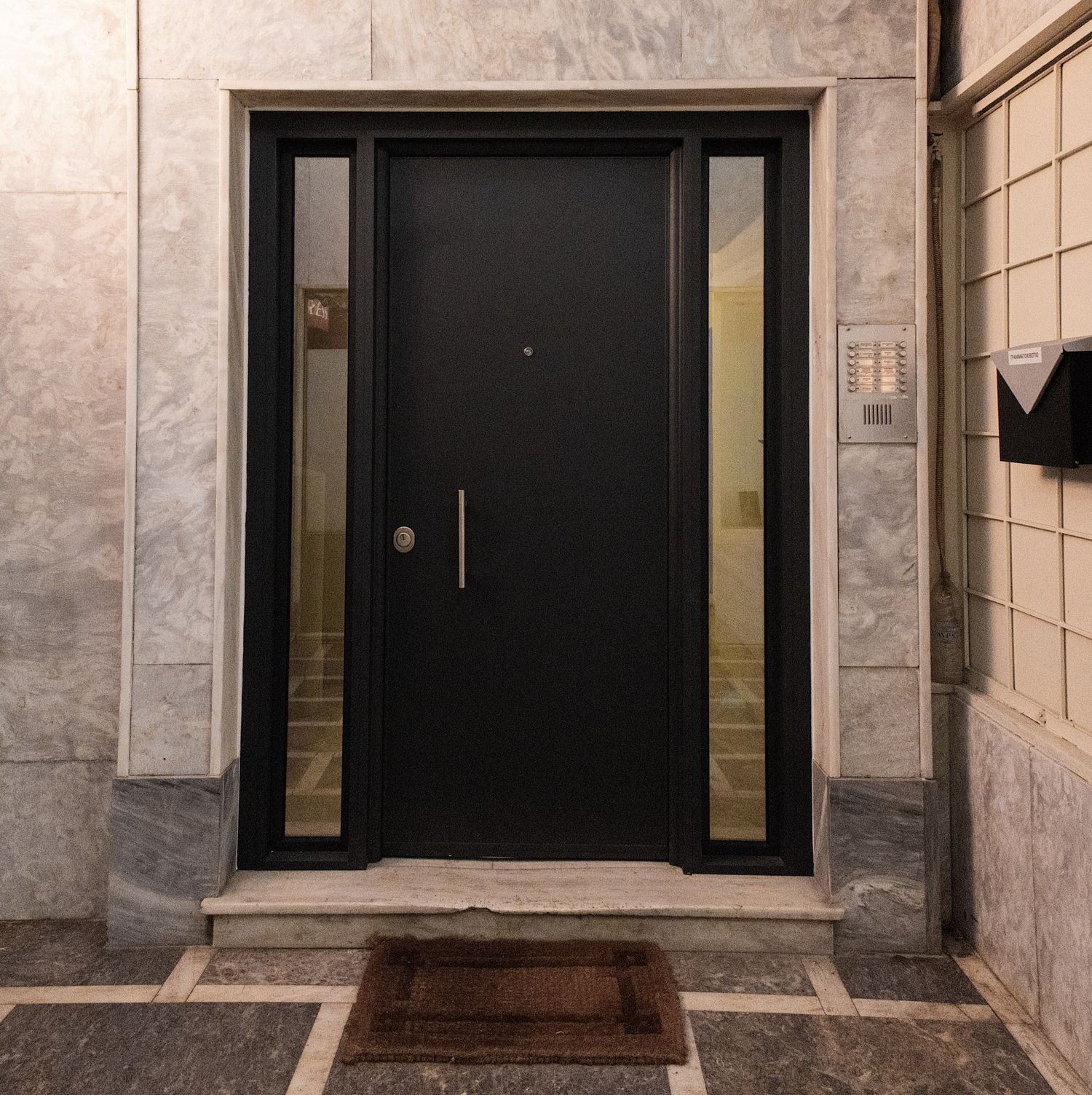 A modern hallway interior with marble walls and black framed glass doors shows a sleek minimalist design aesthetic.