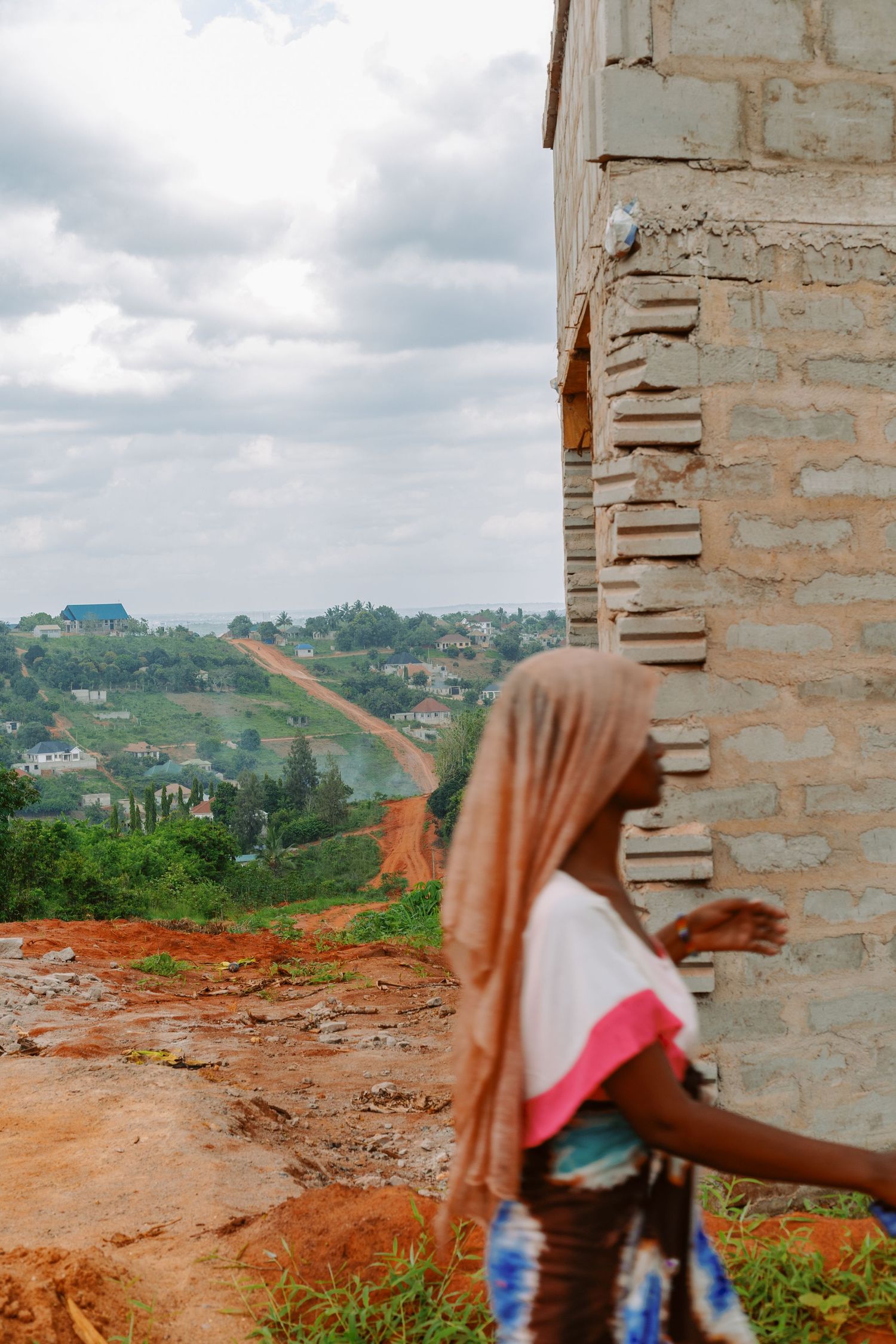Woman standing on an unfinished brick balcony overlooking the landscape, environmental portraiture and storytelling by Naezi Eyes