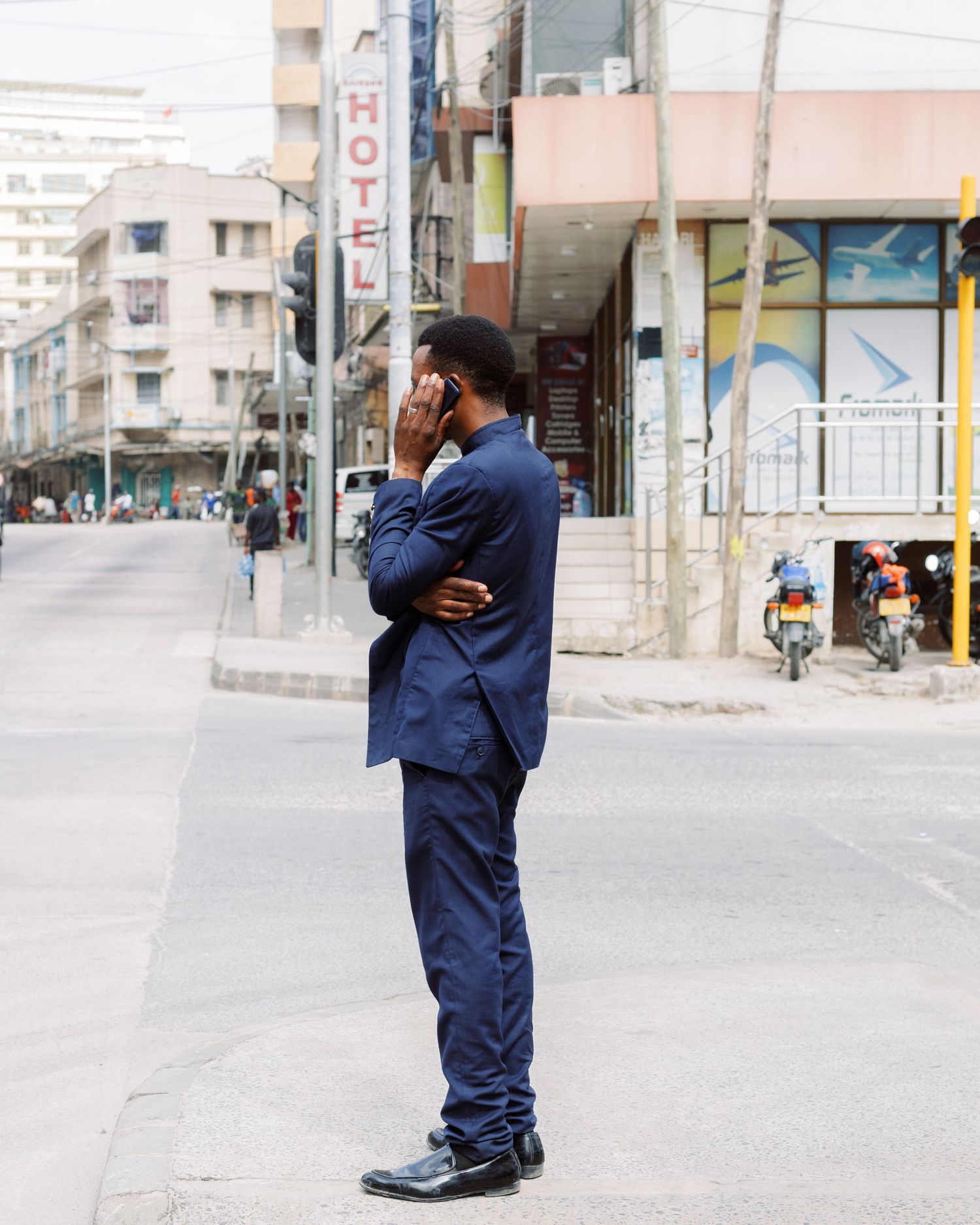 Man in blue suit standing on a street corner in Dar es Salaam, candid corporate street photography capturing daily life.