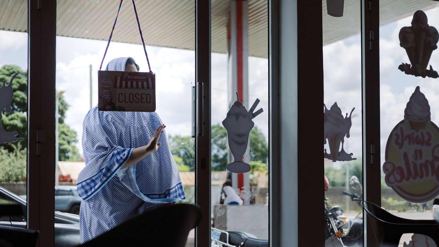 Abstract composition of a woman standing behind a glass door with a closed sign, exploring privacy and barriers in urban Morogoro.