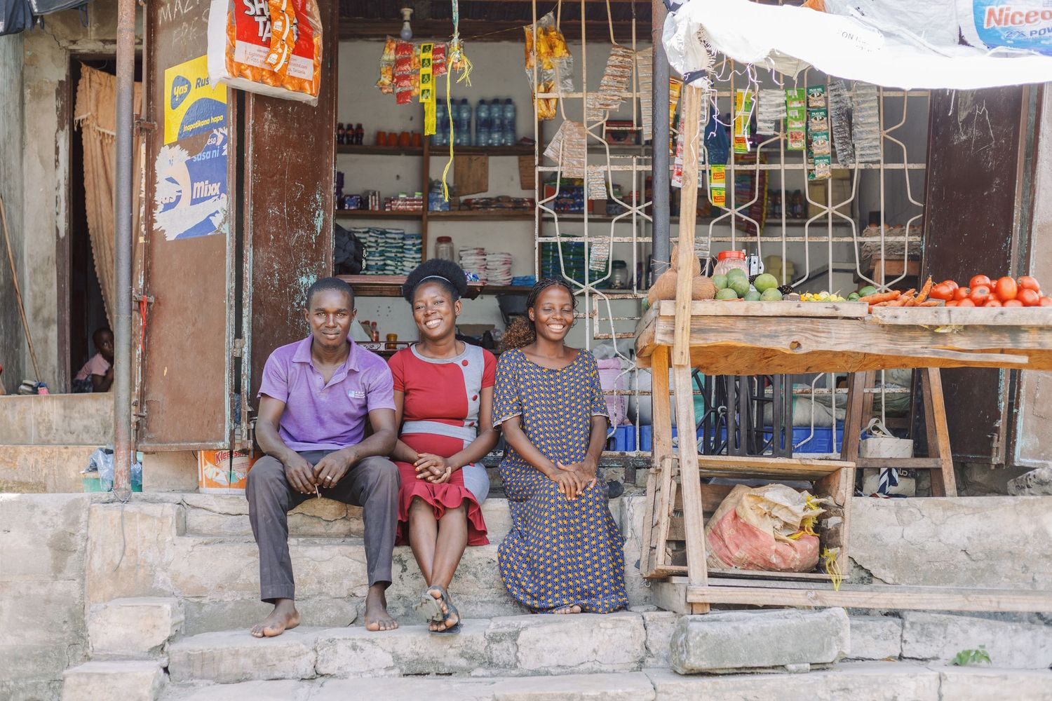 Local shop owners sitting outside their business, capturing the impact of microfinance on daily life in Tanzania by Naezi Eyes.