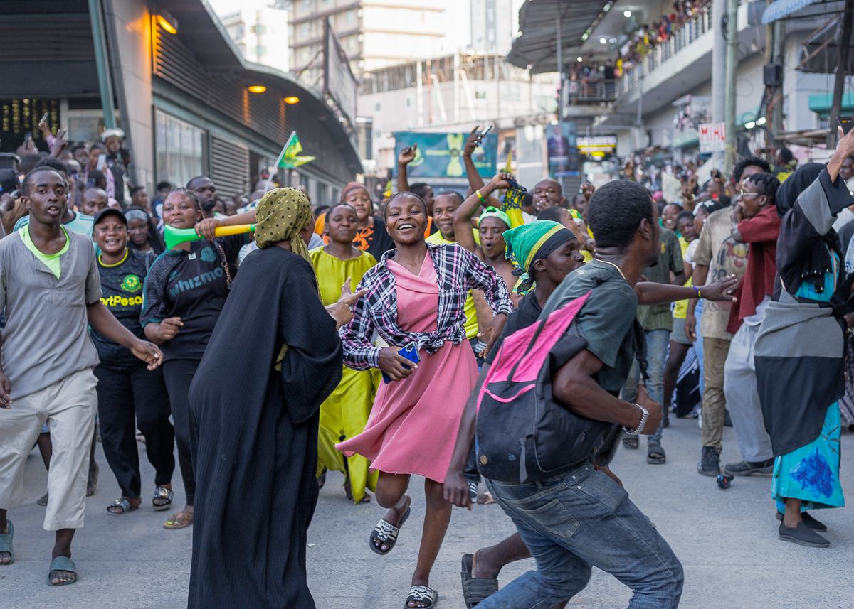 Candid documentary shot of a woman in a pink dress dancing with joy in a street crowd, capturing the vibrant energy and unscripted culture