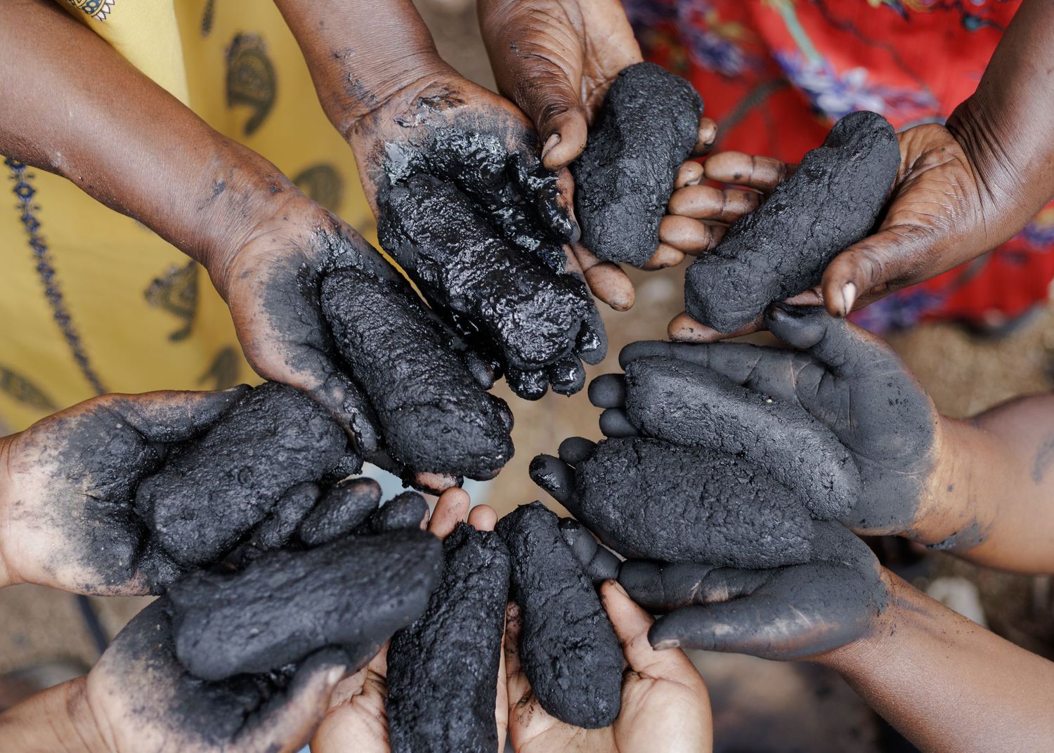 Hands of VICOBA women holding organic charcoal briquettes, sustainable green energy business initiated by female entrepreneurs in Tanzania.