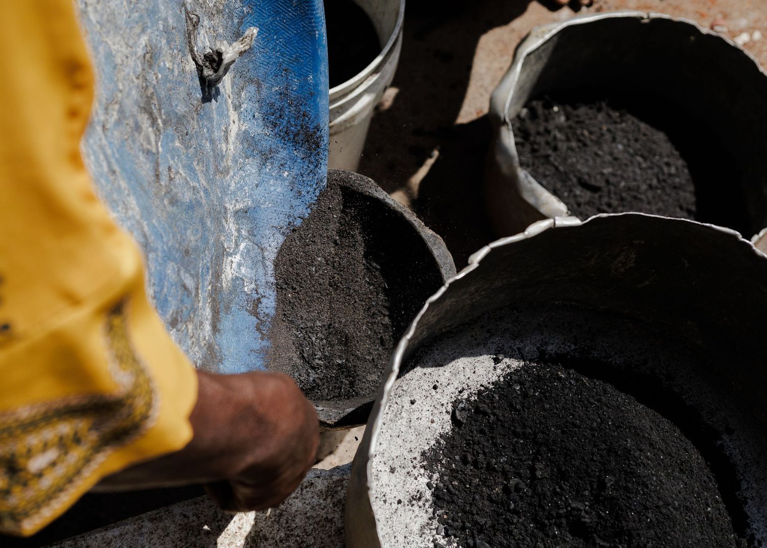Woman processing organic materials for charcoal production, documenting the transition to eco-friendly fuel sources in Africa by Naezi Eyes.