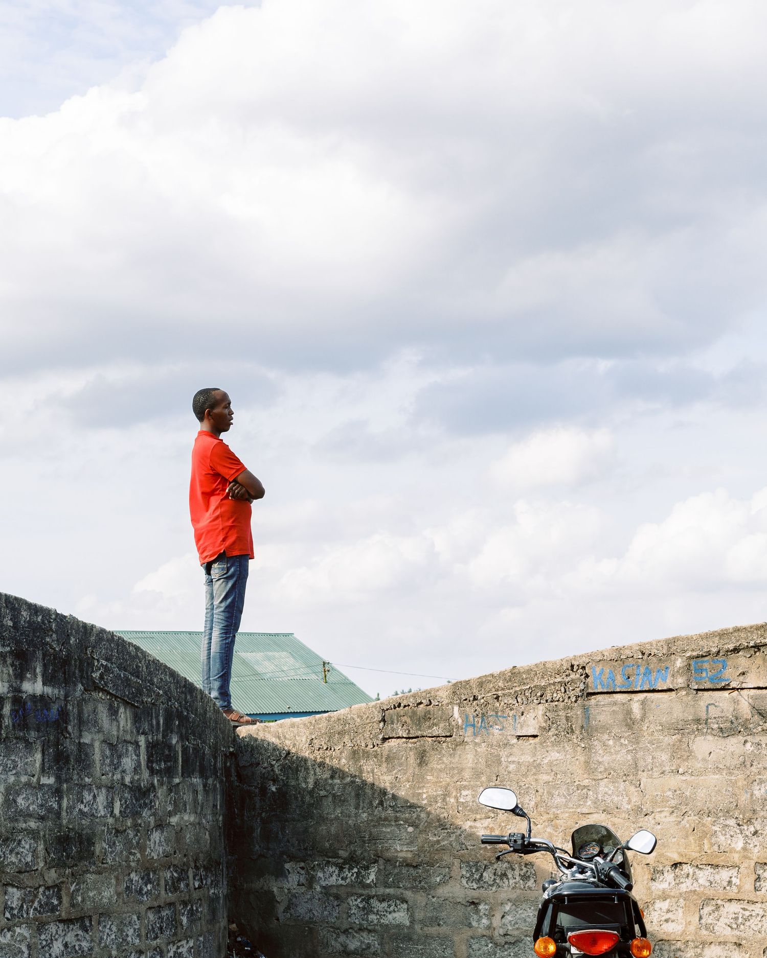 Man in red shirt standing on an elevated wall looking at the sky, minimalist street photography composition by Naezi Eyes