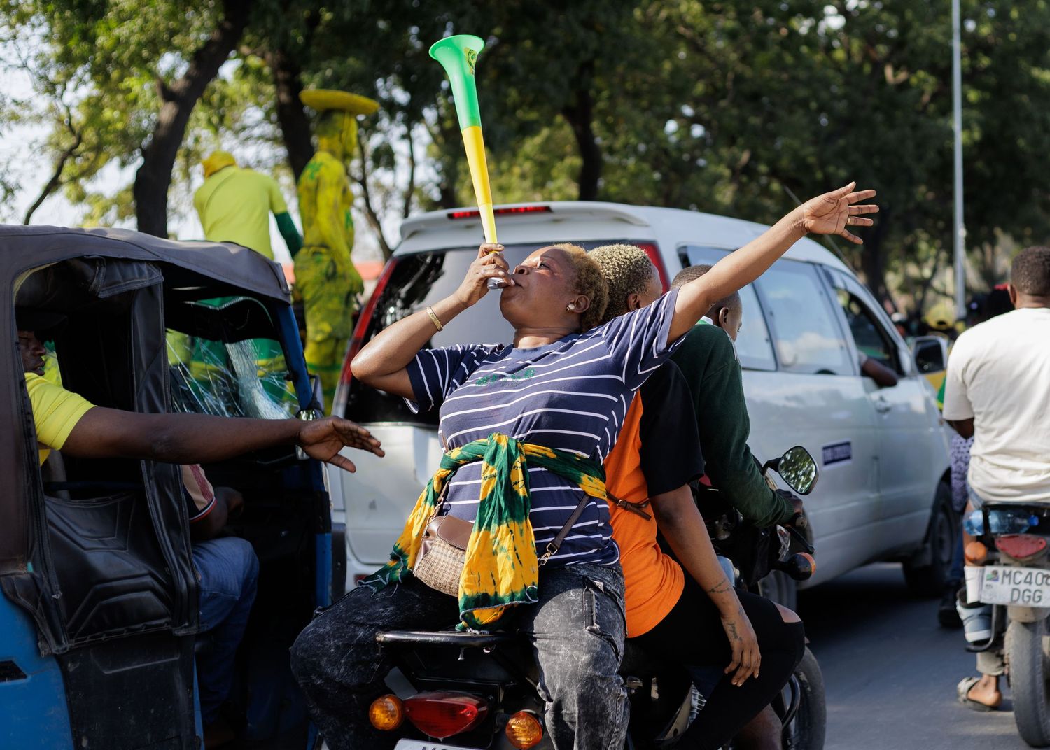 Woman blowing a vuvuzela horn on the back of a motorcycle taxi, capturing the energetic street culture of Dar es Salaam by Naezi Eyes.