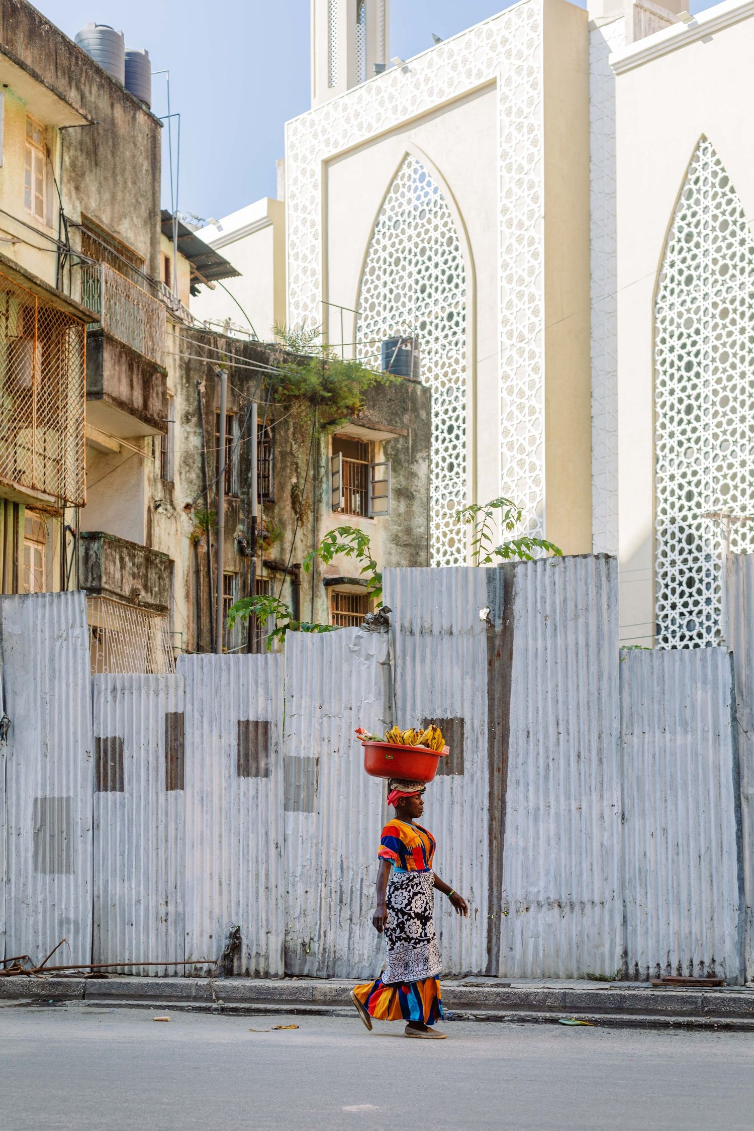 Woman carrying a basket on her head passing a mosque, unscripted documentary photography of Swahili culture in Tanzania.
