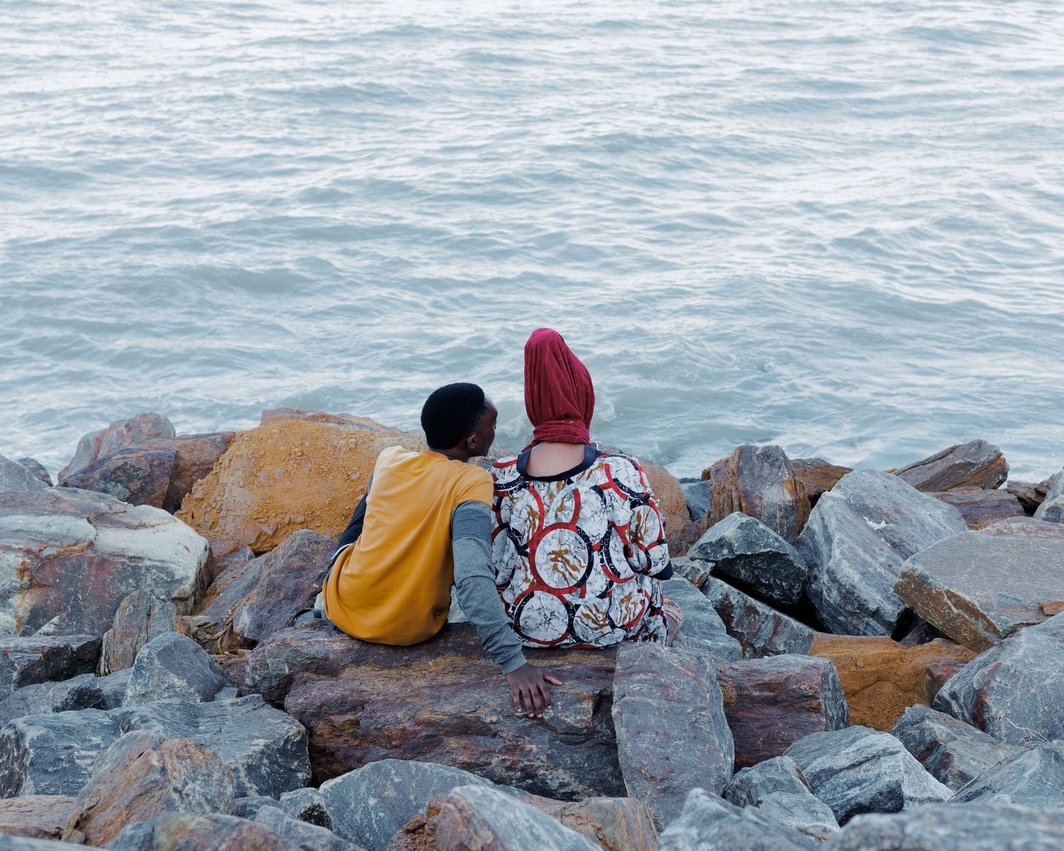 Back view of a couple sitting on sea rocks facing the Indian Ocean, emotive fine art photography focusing on body language and intimacy.