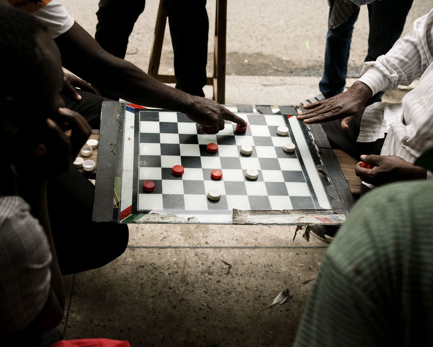 Close up of hands playing a street checkers game, focusing on texture and social connection without showing faces, documentary detail photog