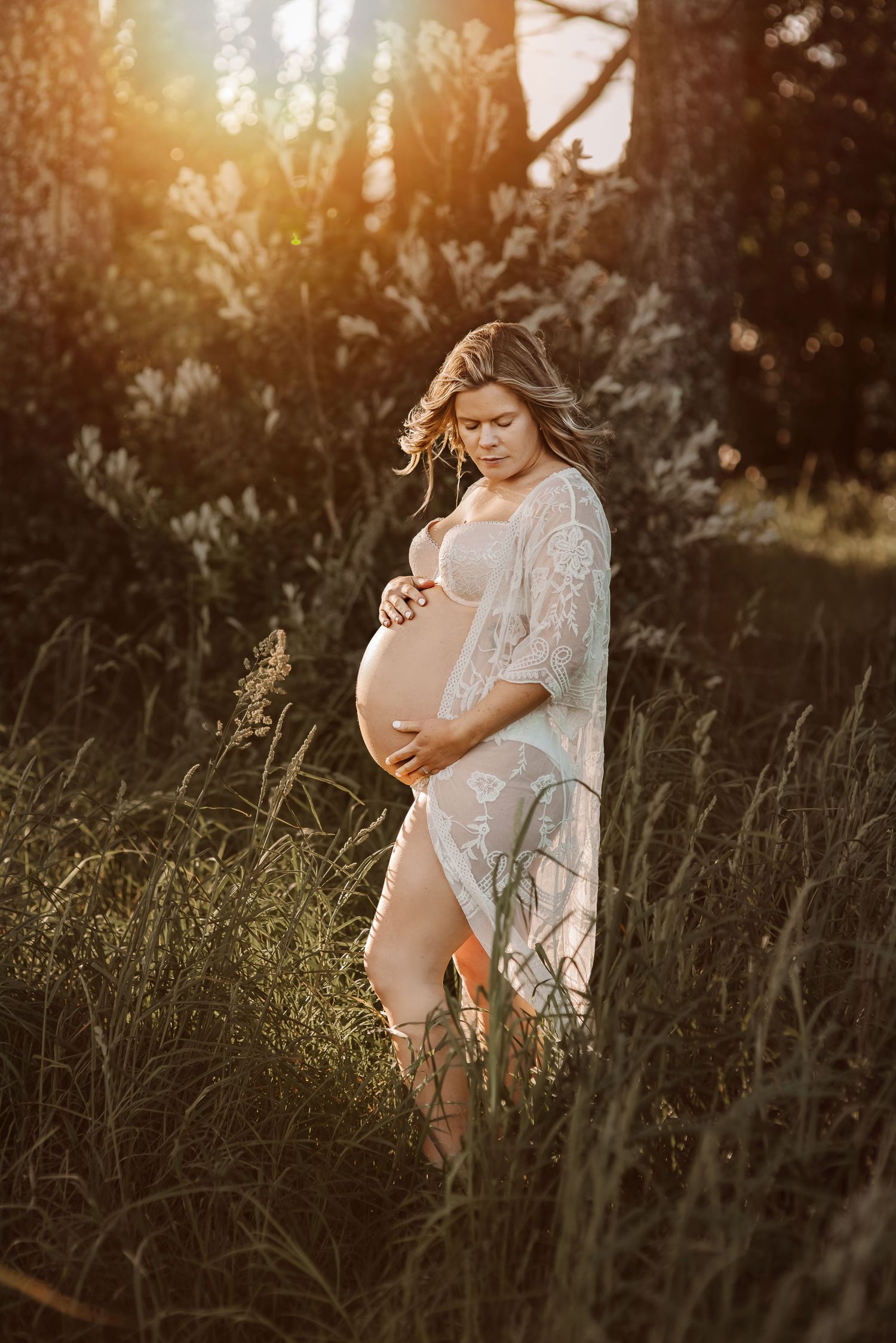 Ethereal maternity portrait in lace dress during golden hour in a wild grass meadow.