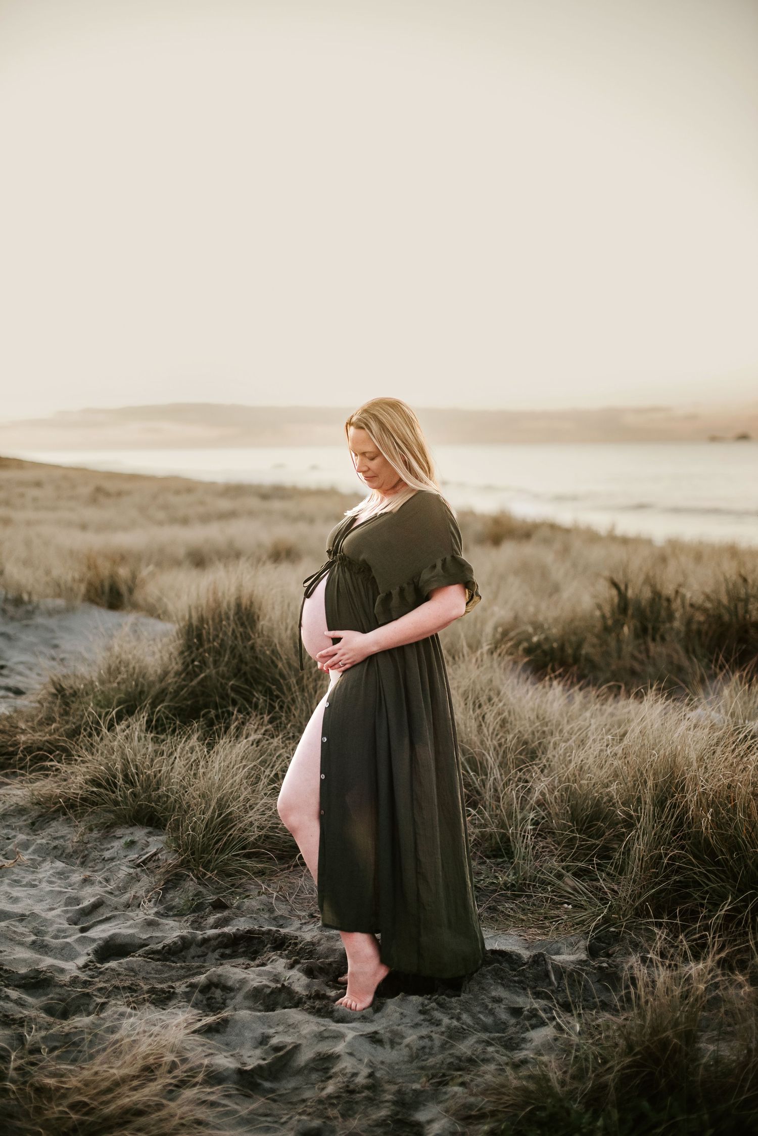 A sunset maternity portrait on a beach with coastal grasses in the foreground.